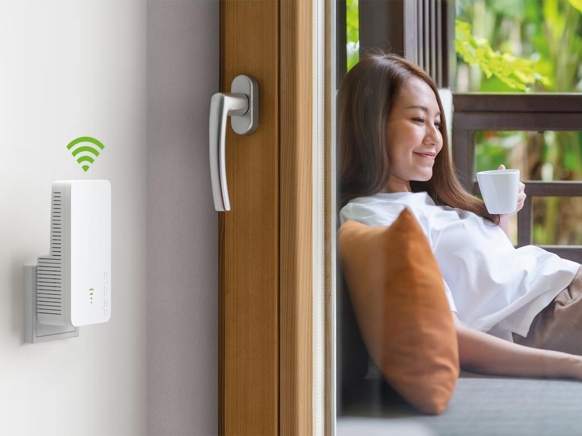 Ein WLAN-Verstärker steckt in der Wand, während eine Frau auf einem Balkon entspannt.