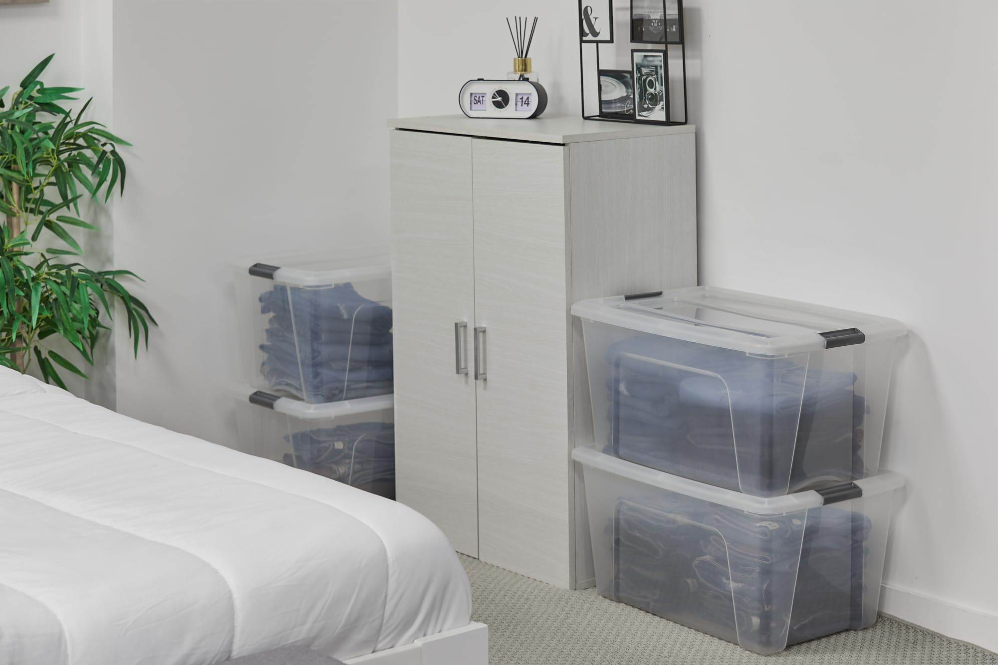 Un armadio bianco, scatole di plastica impilate piene di vestiti e parte di un letto in una stanza luminosa.