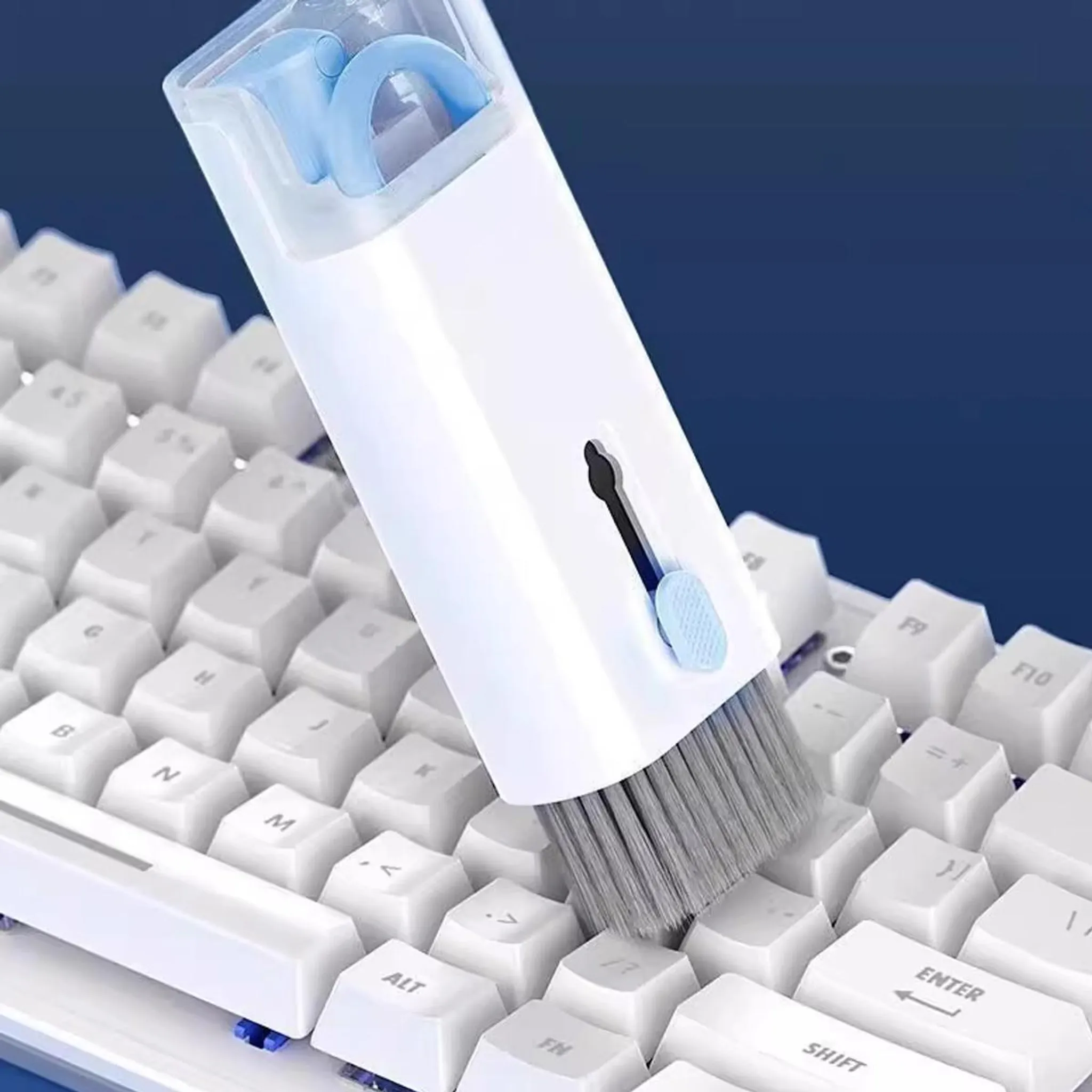Ein weiß-blaues Reinigungsset mit Pinsel säubert die weißen Tasten einer Computertastatur vor dunklem Hintergrund.