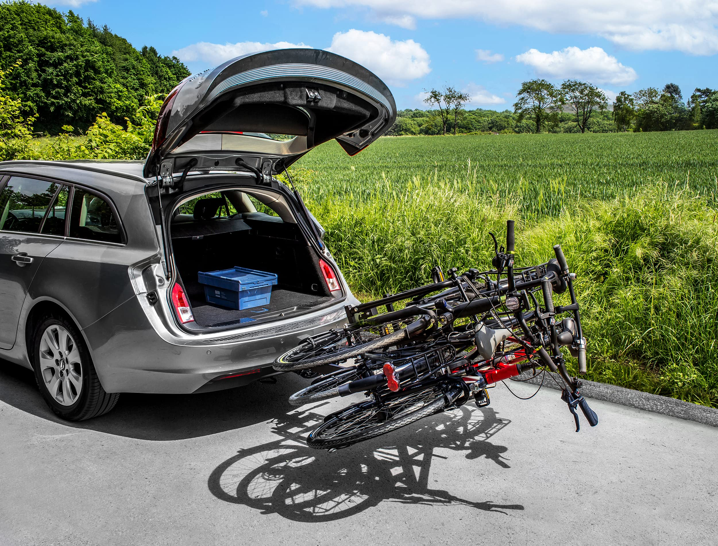 Station wagon grigia con bagagliaio aperto e portabici con due biciclette parcheggiata vicino a un prato.
