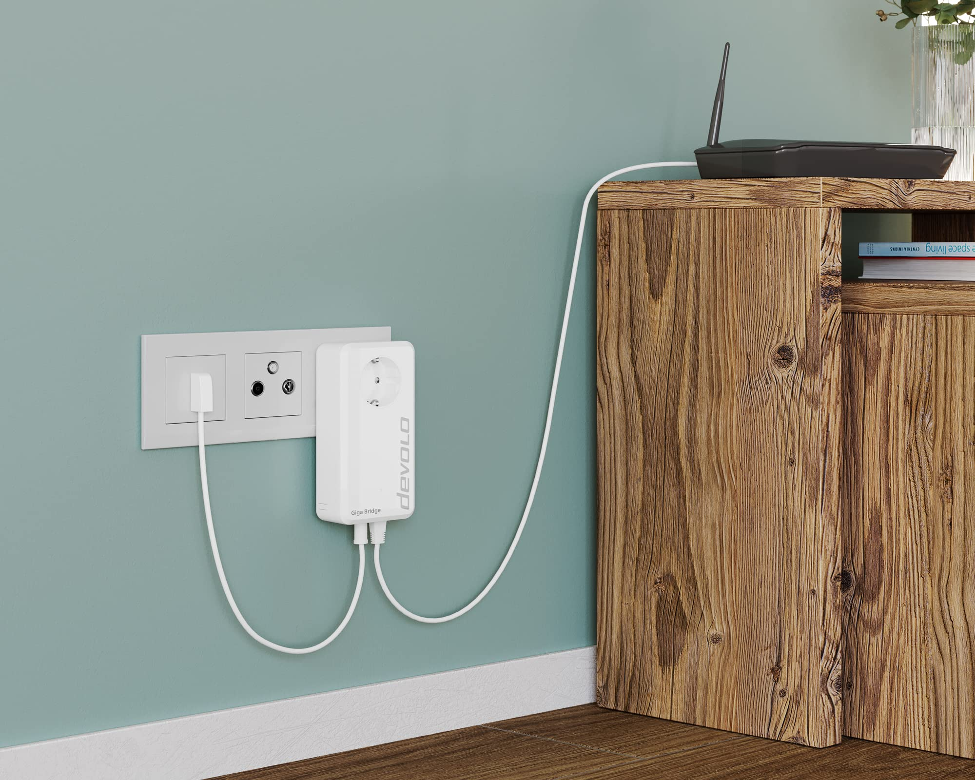 Un devolo Giga Bridge bianco inserito in una presa a muro, collegato via cavo a un router su un mobile in legno.