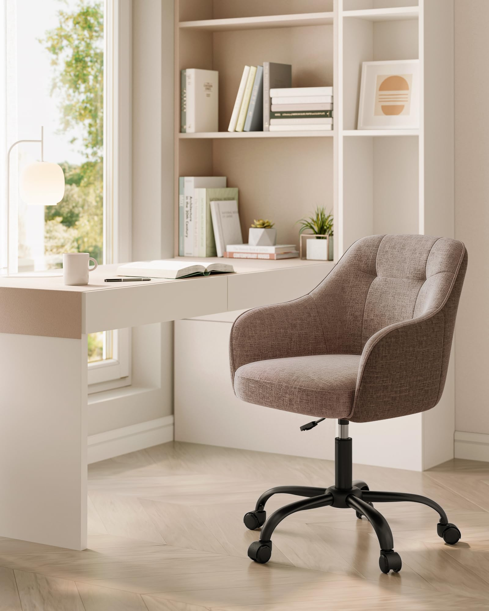 Ein moderner grauer Bürostuhl steht neben einem weißen Schreibtisch mit Büchern, Lampe und Fensterlicht.