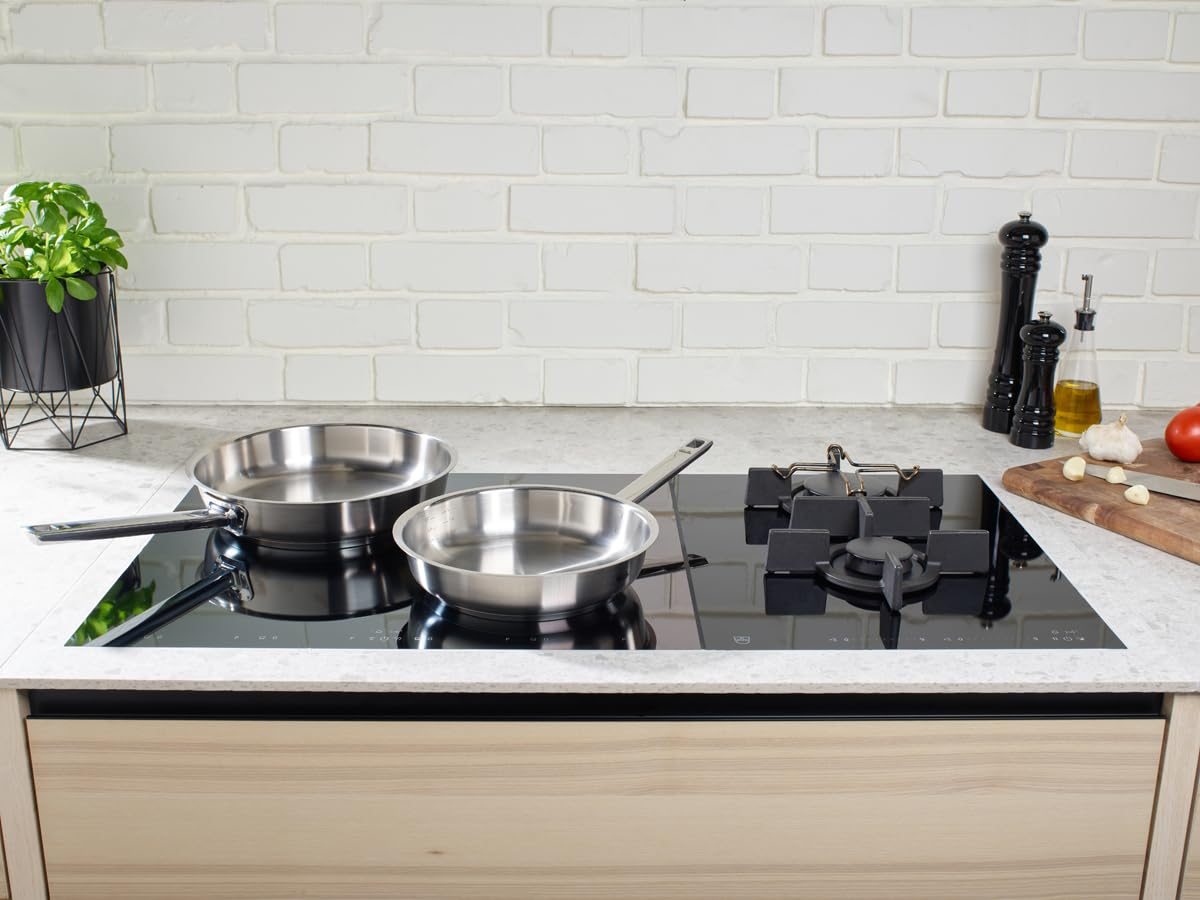 Deux poêles en acier inoxydable sur une table de cuisson à induction noire devant un mur de briques.