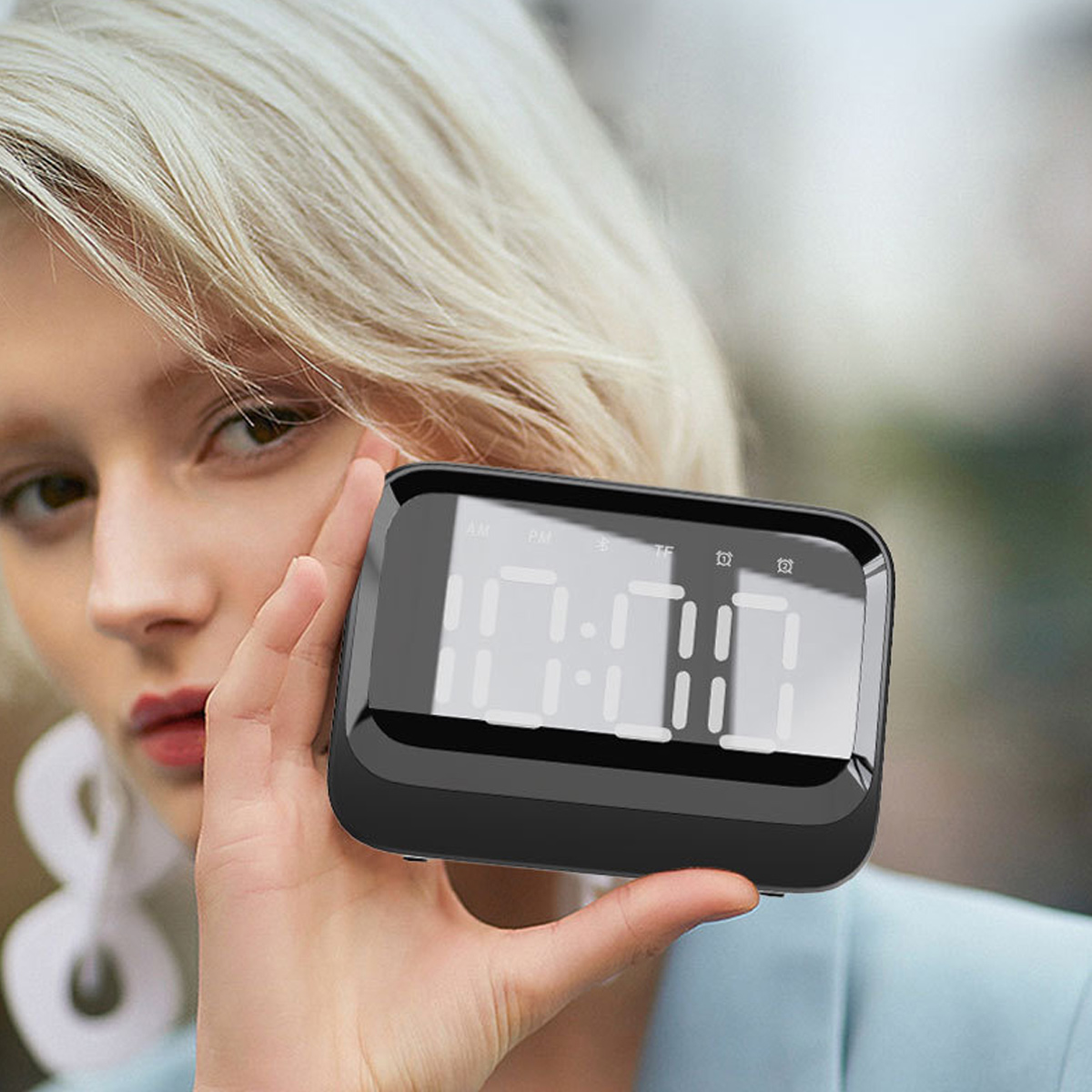 Eine blonde Frau hält eine kleine, schwarze Digitaluhr mit beleuchtetem Display in der Hand.