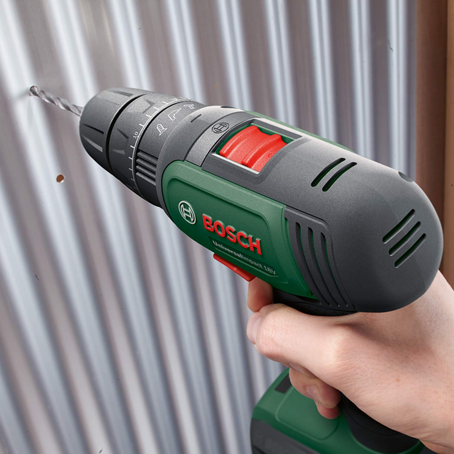 Una mano tiene un trapano a batteria Bosch verde e nero mentre fora una lamiera.