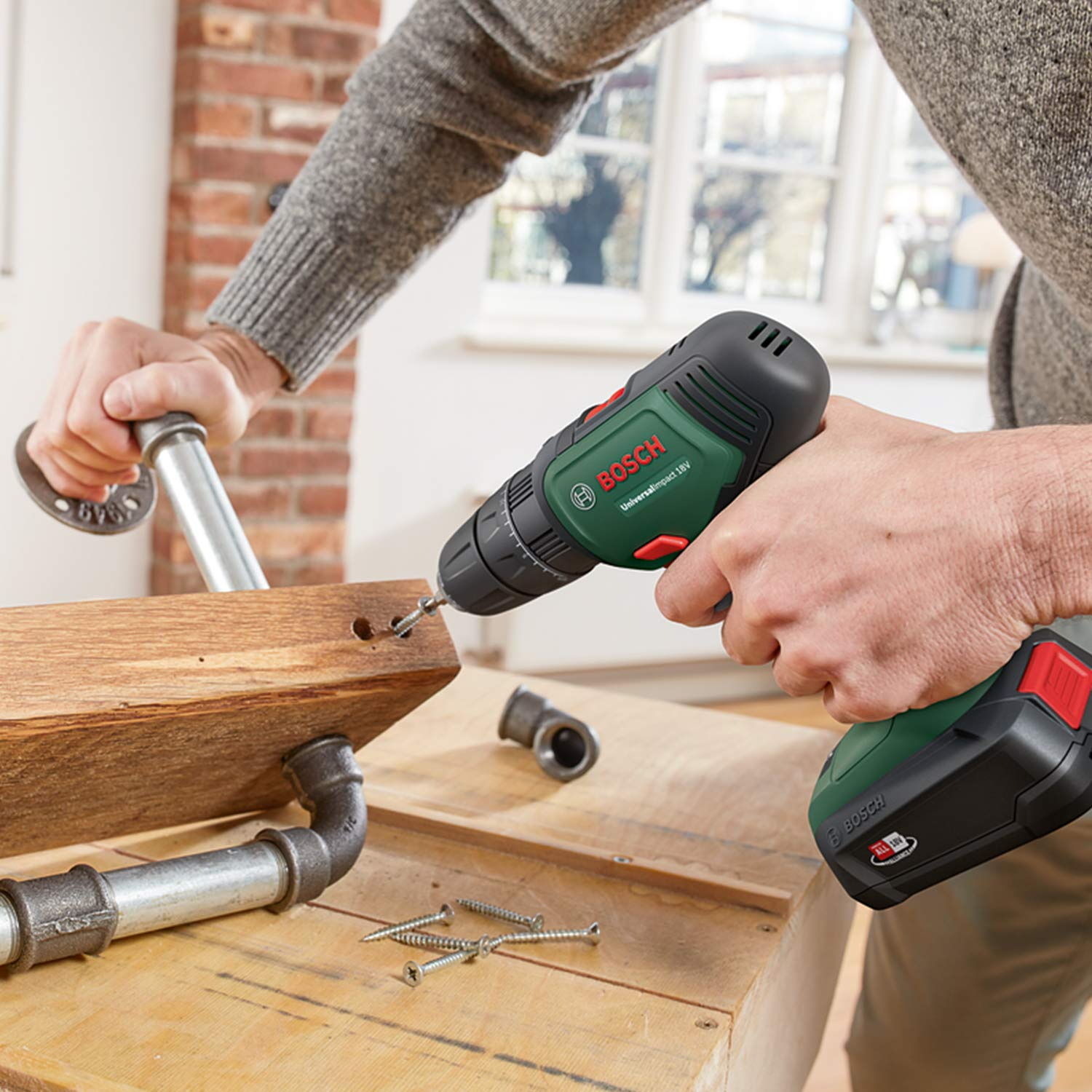 Una persona usa un trapano a batteria Bosch verde per avvitare un pezzo di legno su un banco.