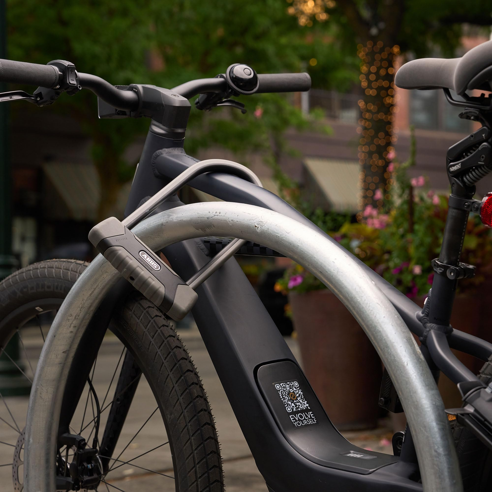 Un vélo électrique noir attaché à un support métallique avec un antivol en U à l'extérieur.
