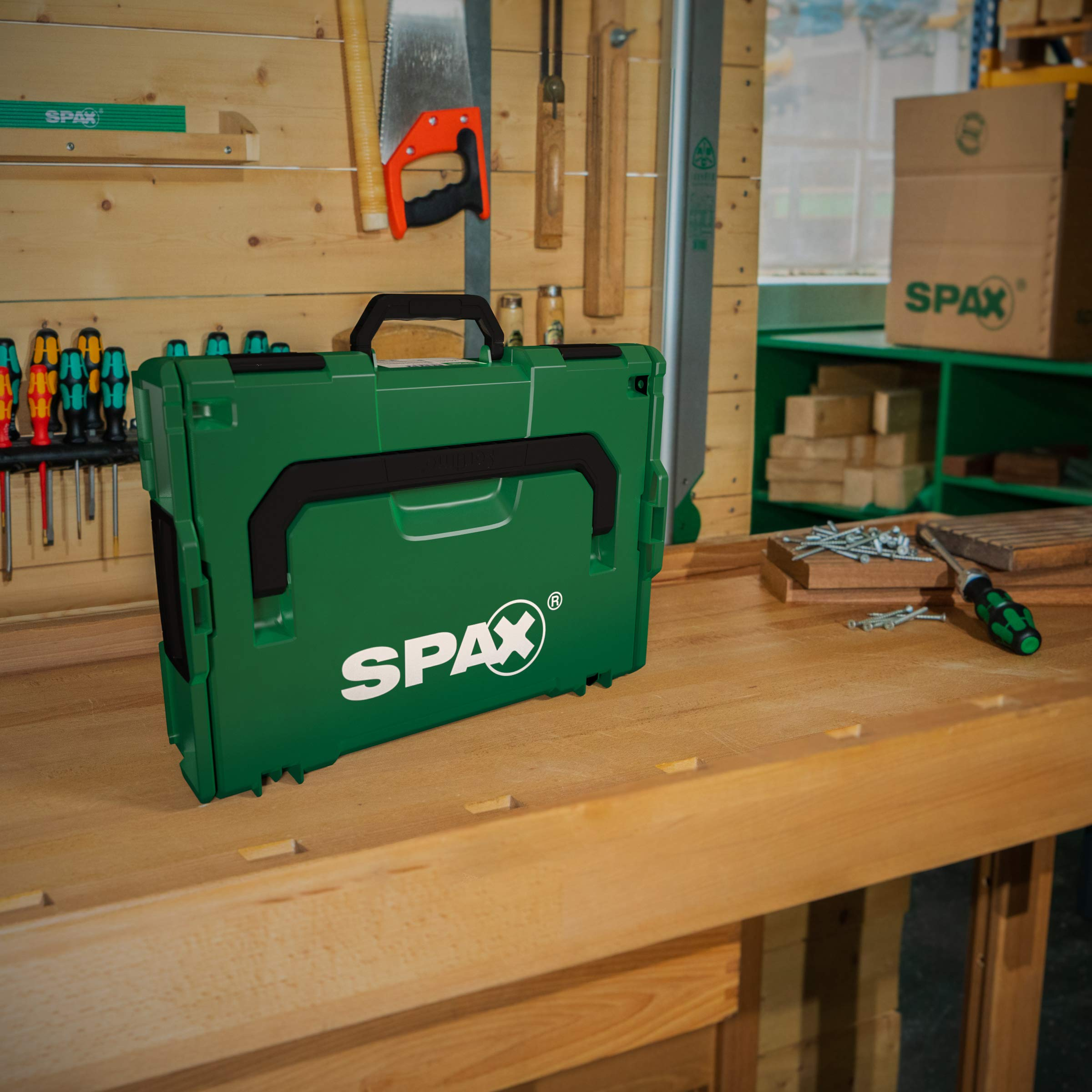 Una cassetta degli attrezzi verde Spax si trova su un banco da lavoro in legno.