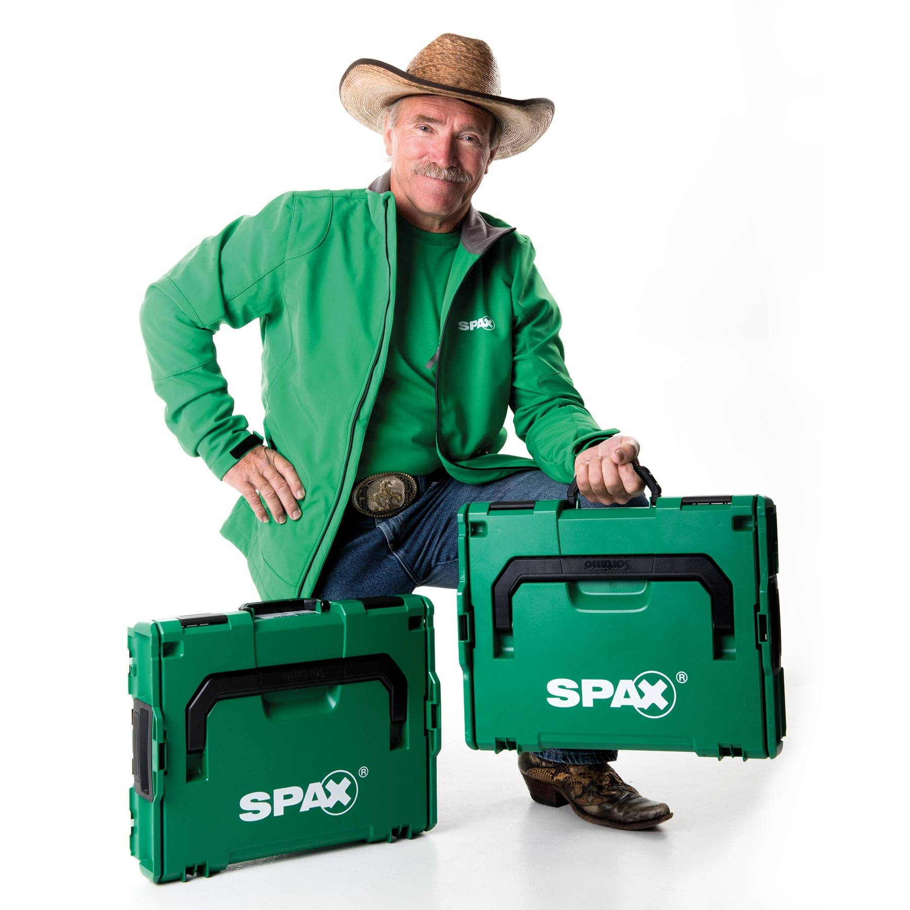 Un uomo con cappello da cowboy e giacca verde tiene valigette portautensili Spax verdi.