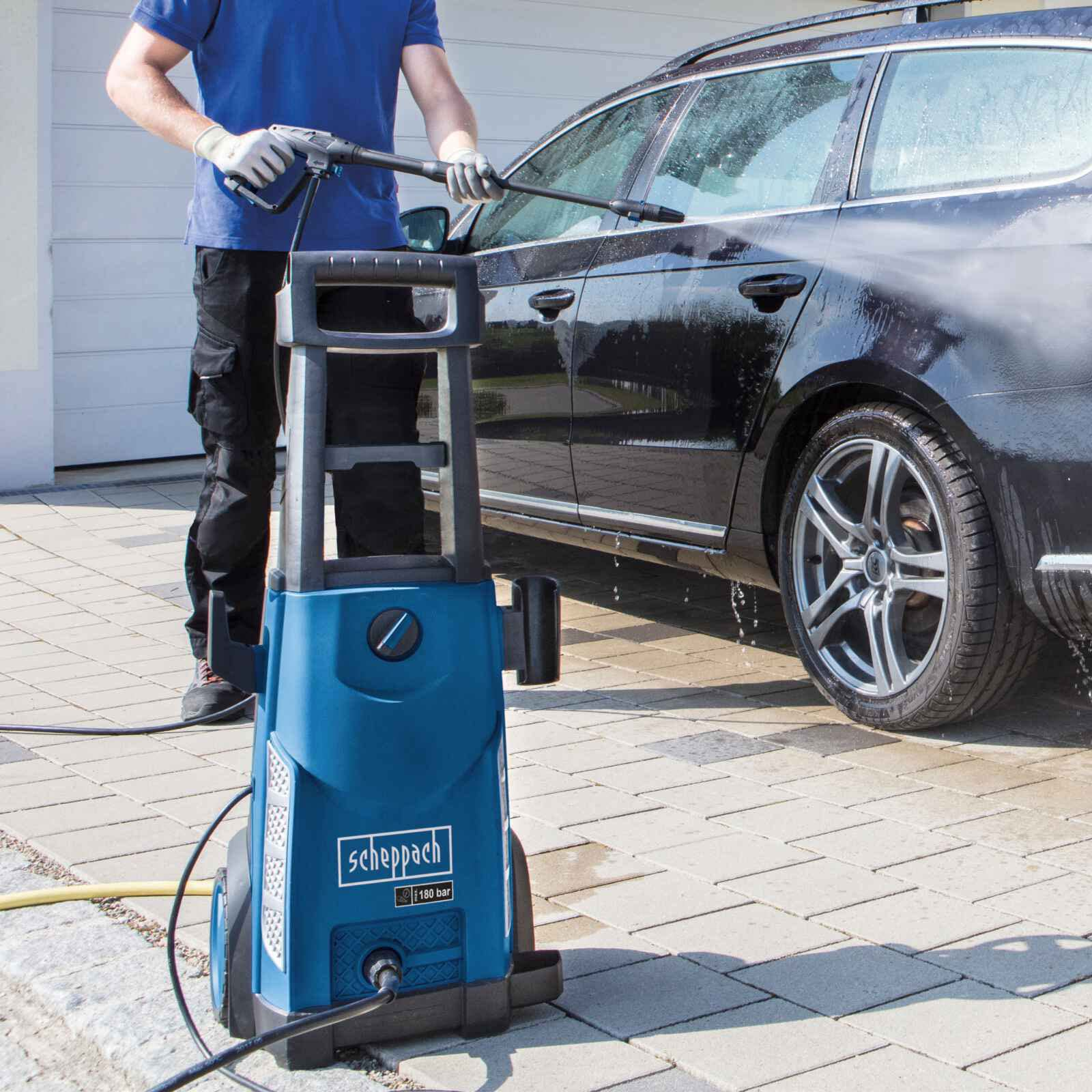 Ein Mann wäscht ein schwarzes Auto mit einem blauen Scheppach-Hochdruckreiniger.