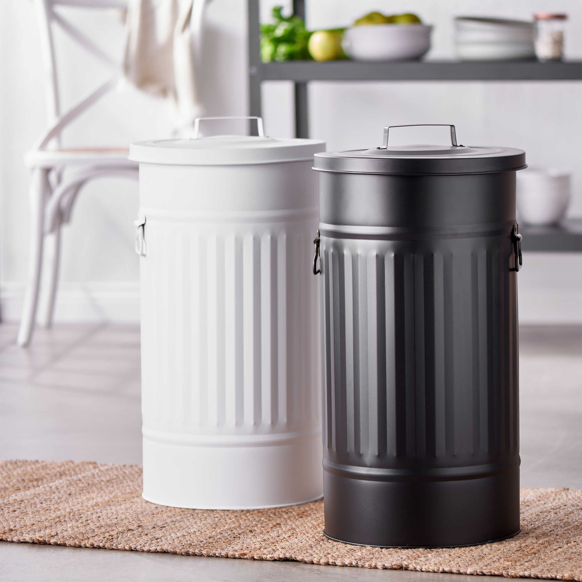 Deux poubelles en métal, une blanche et une noire, se tiennent sur un tapis tissé dans une cuisine moderne.