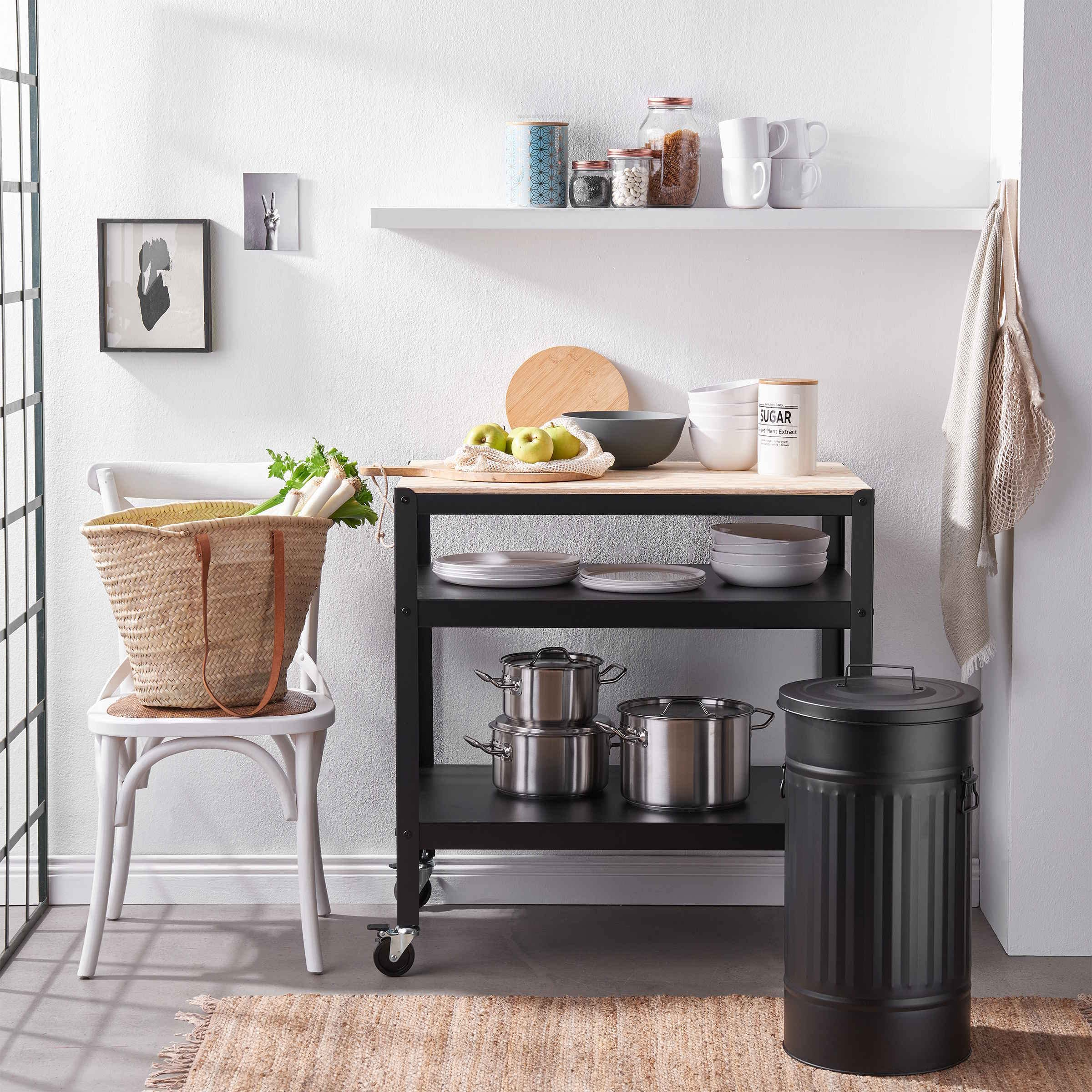 Un îlot de cuisine avec cadre en métal noir et plateau en bois, contenant assiettes, casseroles, pommes et vaisselle.