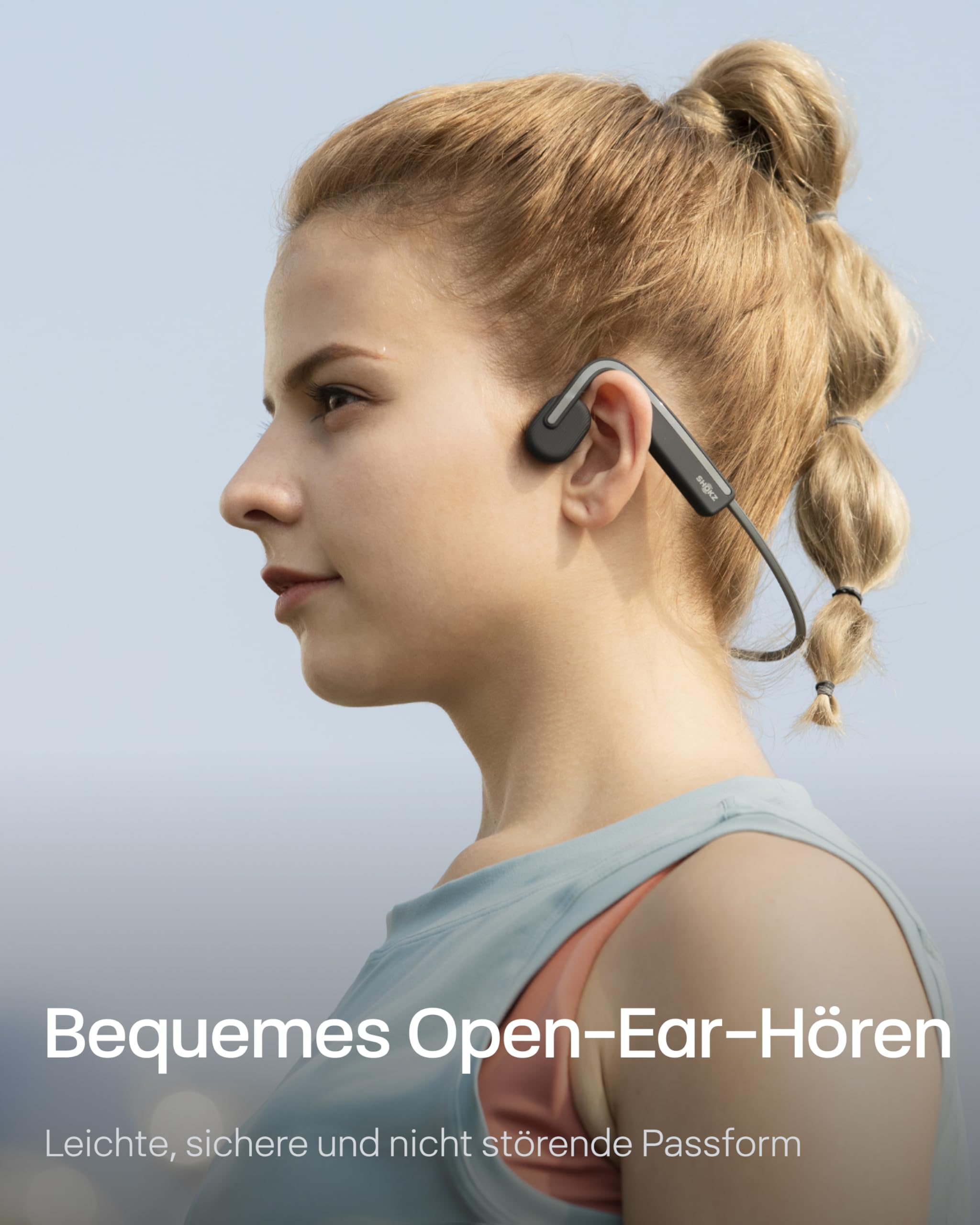 Eine Frau mit blondem Zopf und grauen Open-Ear-Kopfhörern vor hellblauem Hintergrund.