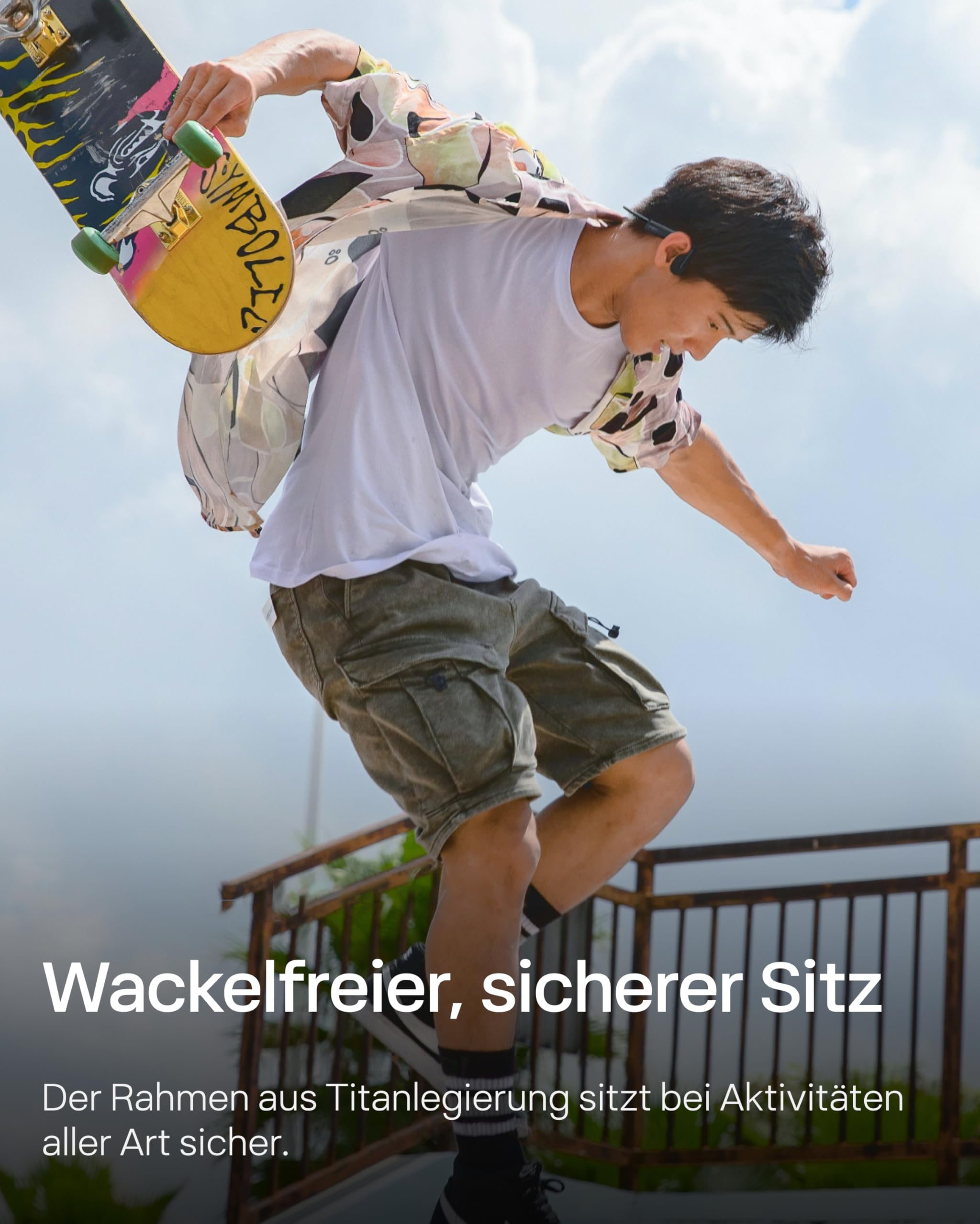 Skater in einem weißen T-Shirt und Shorts springt mit einem bunten Skateboard vor einem Zaun.