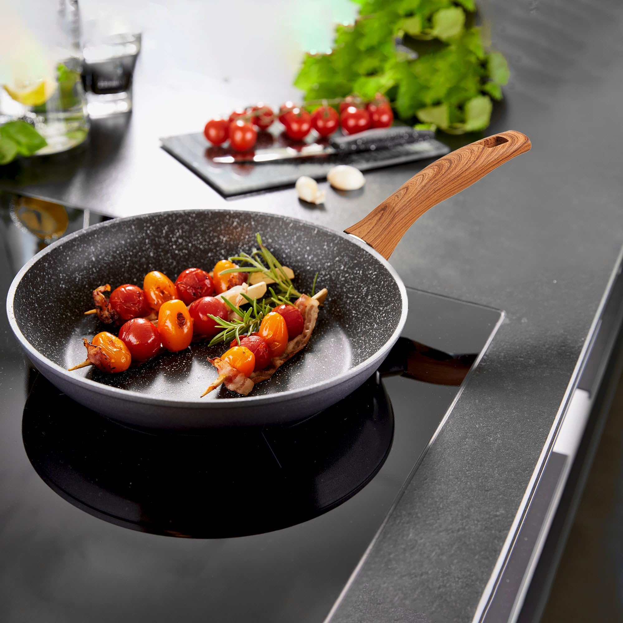 Une poêle à manche en bois sur une cuisinière cuit des brochettes de tomates cerises, de bacon et de romarin.