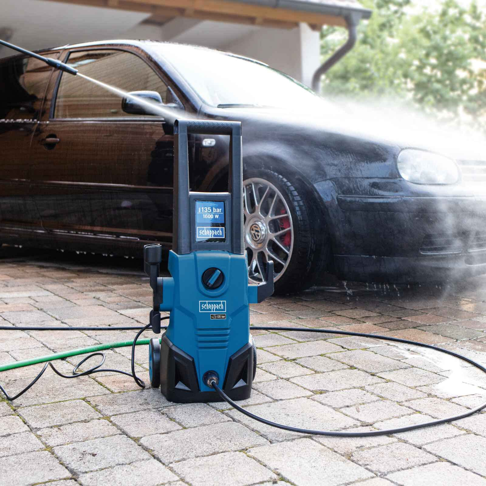 Un'idropulitrice blu è posata su pavé mentre un'auto nera viene lavata sullo sfondo.