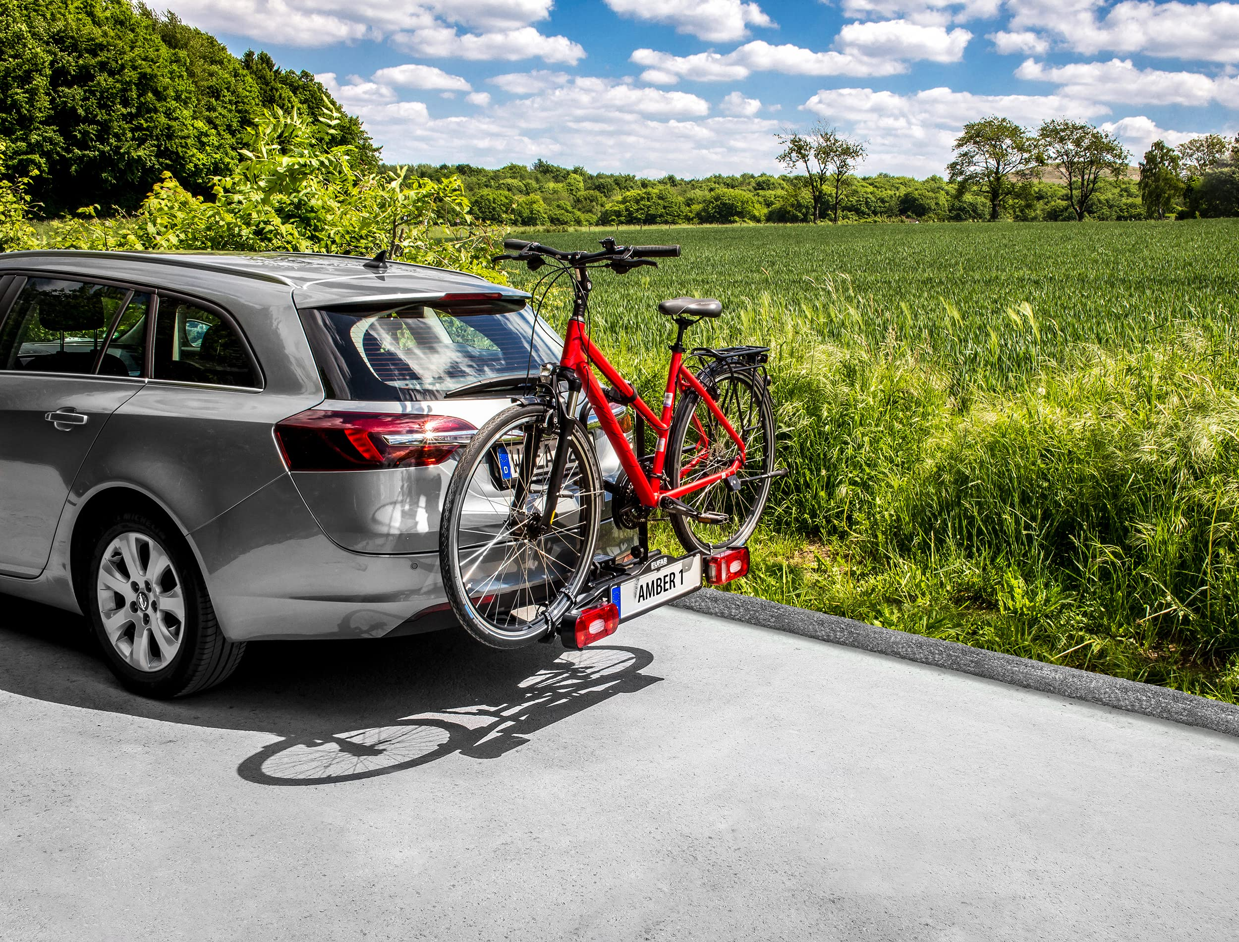 Un'auto argentata con una bicicletta rossa sul portapacchi posteriore parcheggiata vicino a un campo verde.
