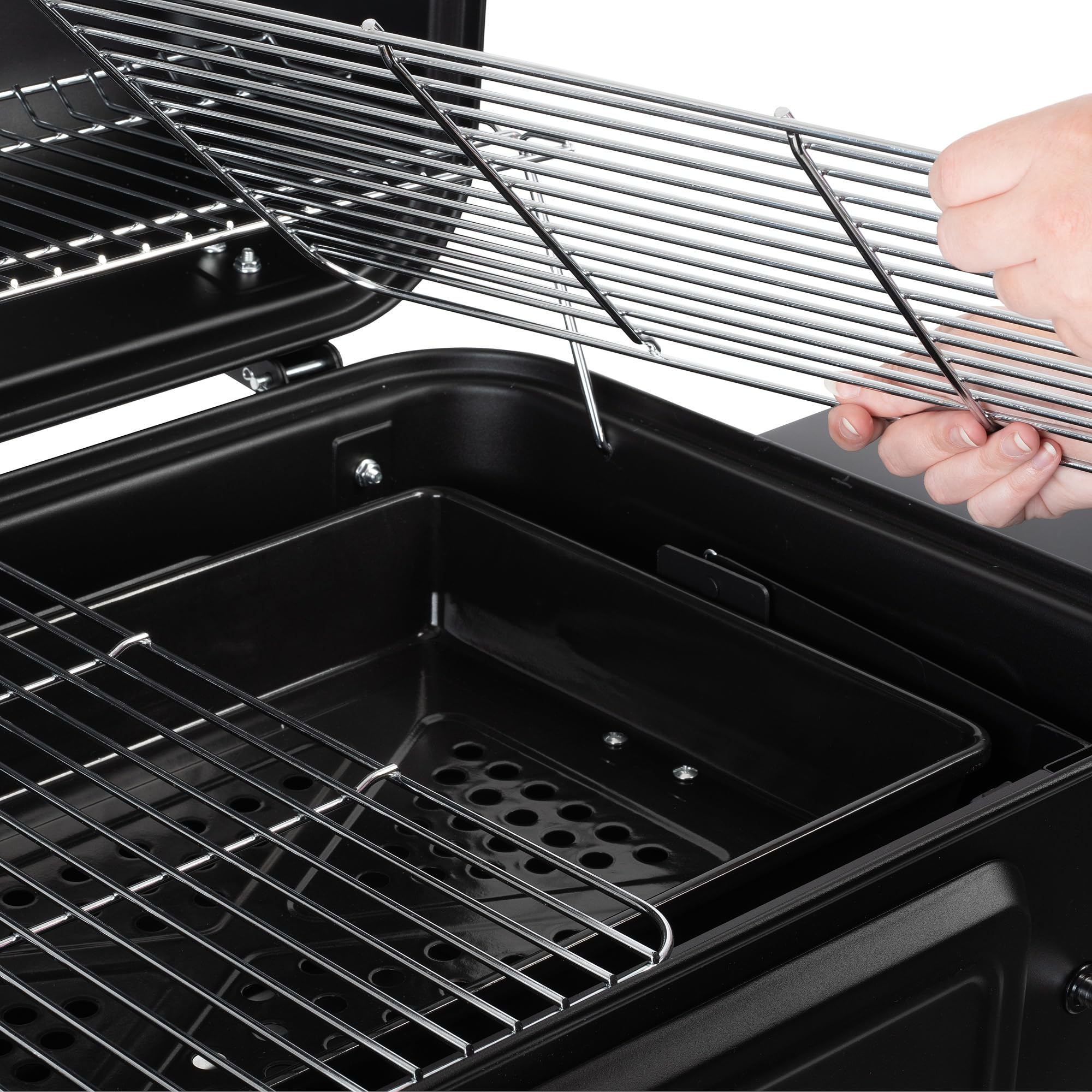 Une paire de mains ajuste les grilles chromées dans un barbecue noir.