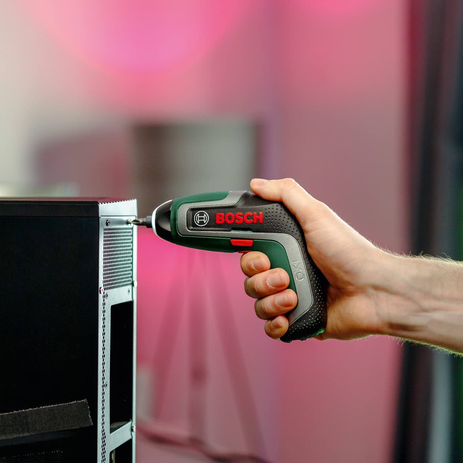 Una mano tiene un avvitatore a batteria Bosch verde, serrando una vite sul retro di un case per computer nero.