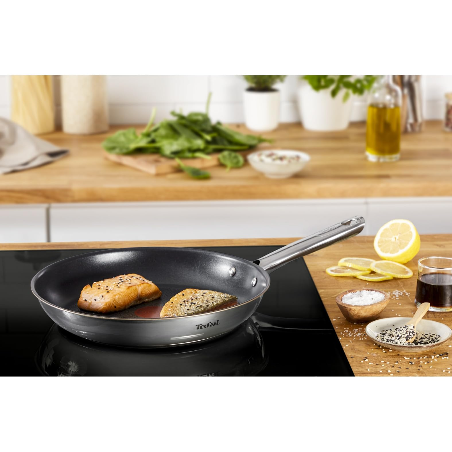 Dos filetes de salmón cocinados en una sartén Tefal en una estufa, con rodajas de limón y especias.