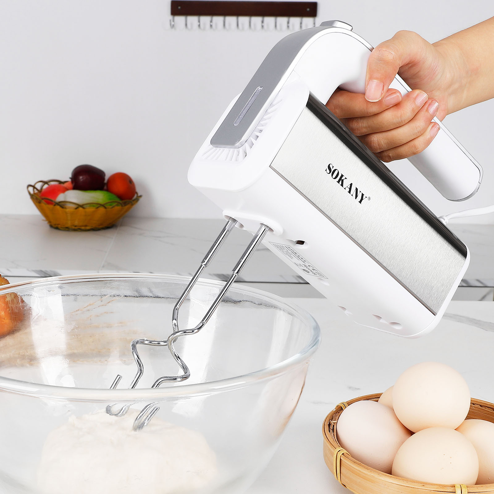 Handmixer mit Knethaken über einer Schüssel Teig und einer Schüssel Eier.