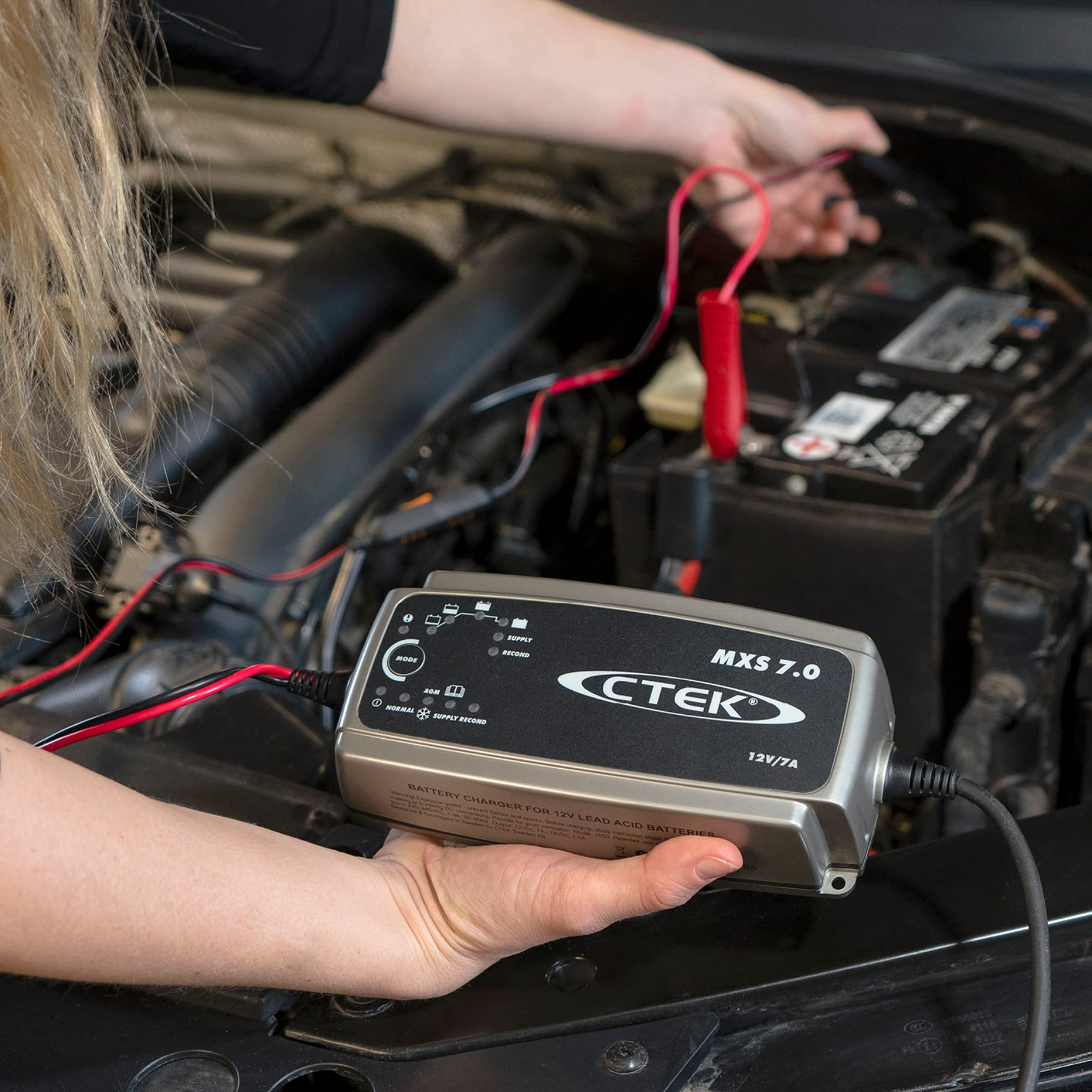 Una persona collega un caricabatterie CTEK MXS 7.0 a una batteria per auto.