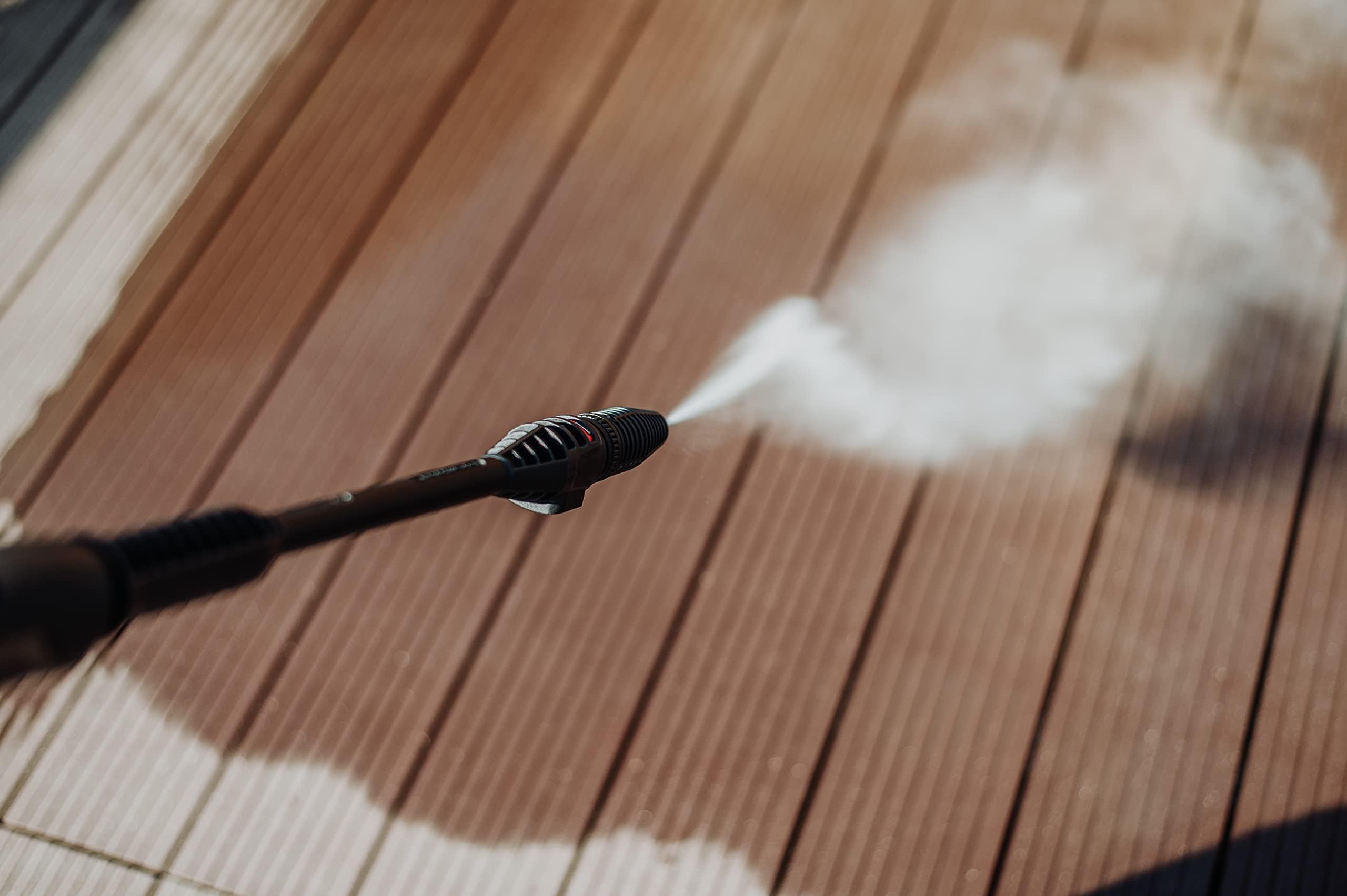 Una idropulitrice spruzza acqua su una terrazza in legno marrone.