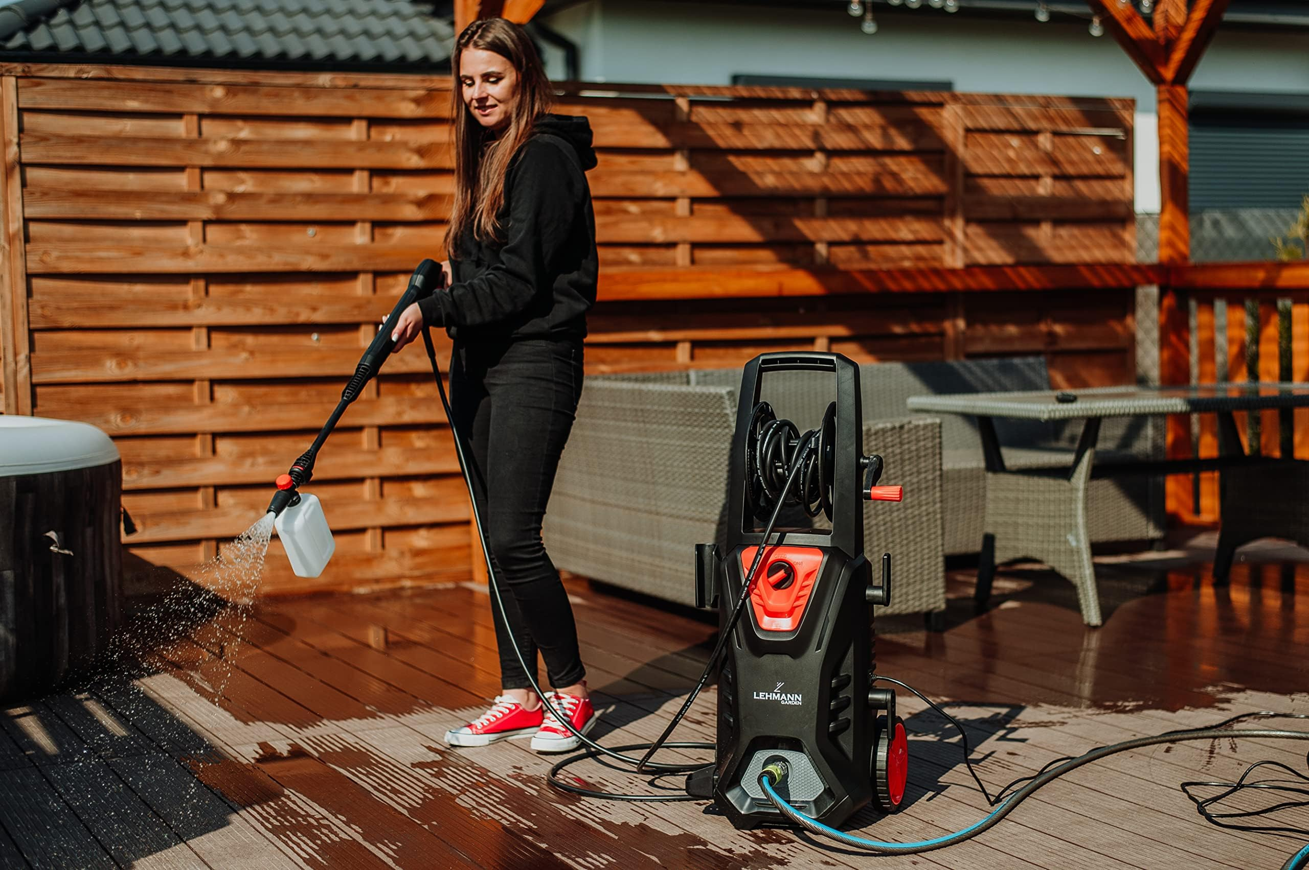 Una donna in abiti neri lava il patio in legno con un idropulitrice.