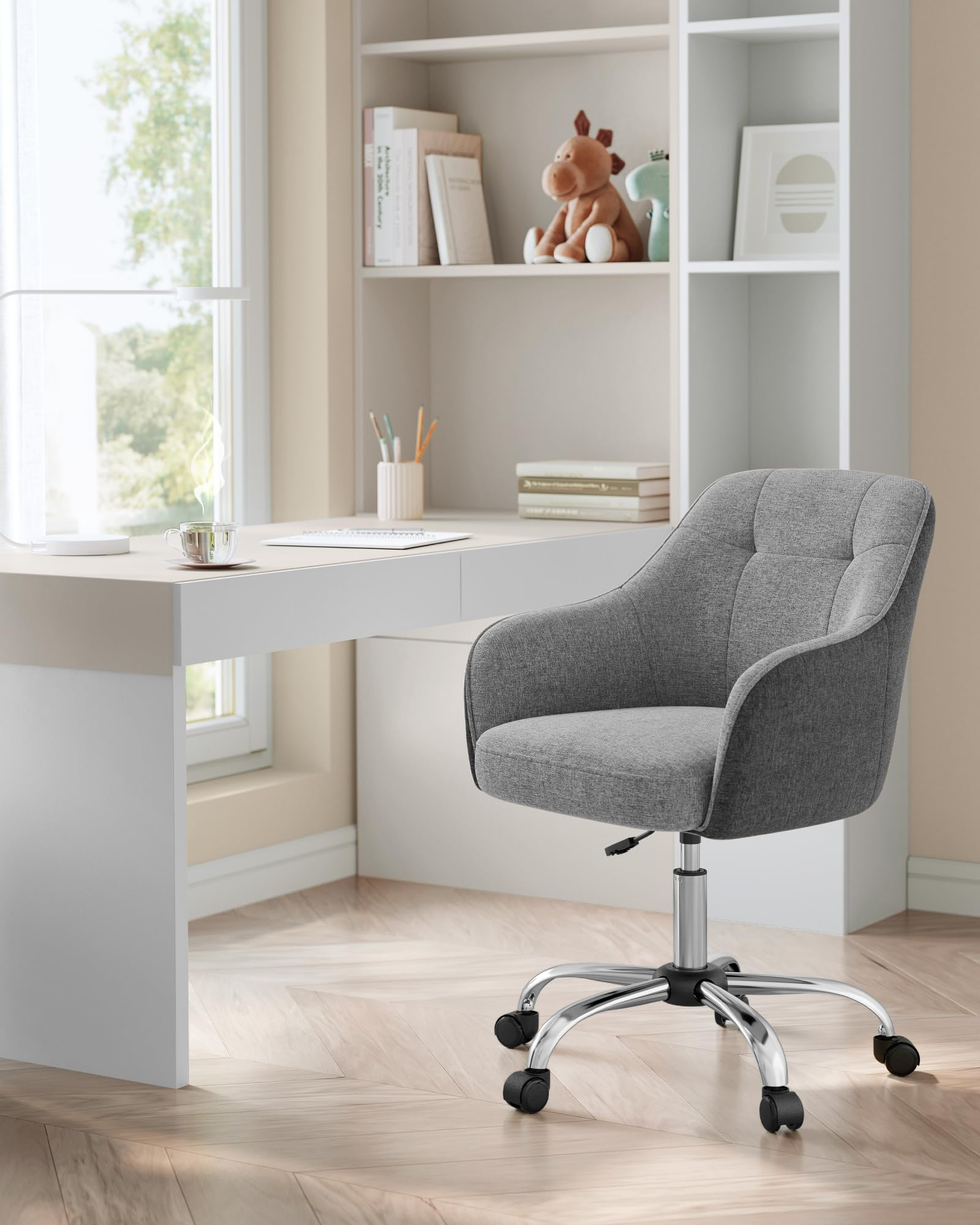 Une chaise de bureau rembourree grise a roulettes se trouve dans une piece lumineuse devant un bureau blanc.