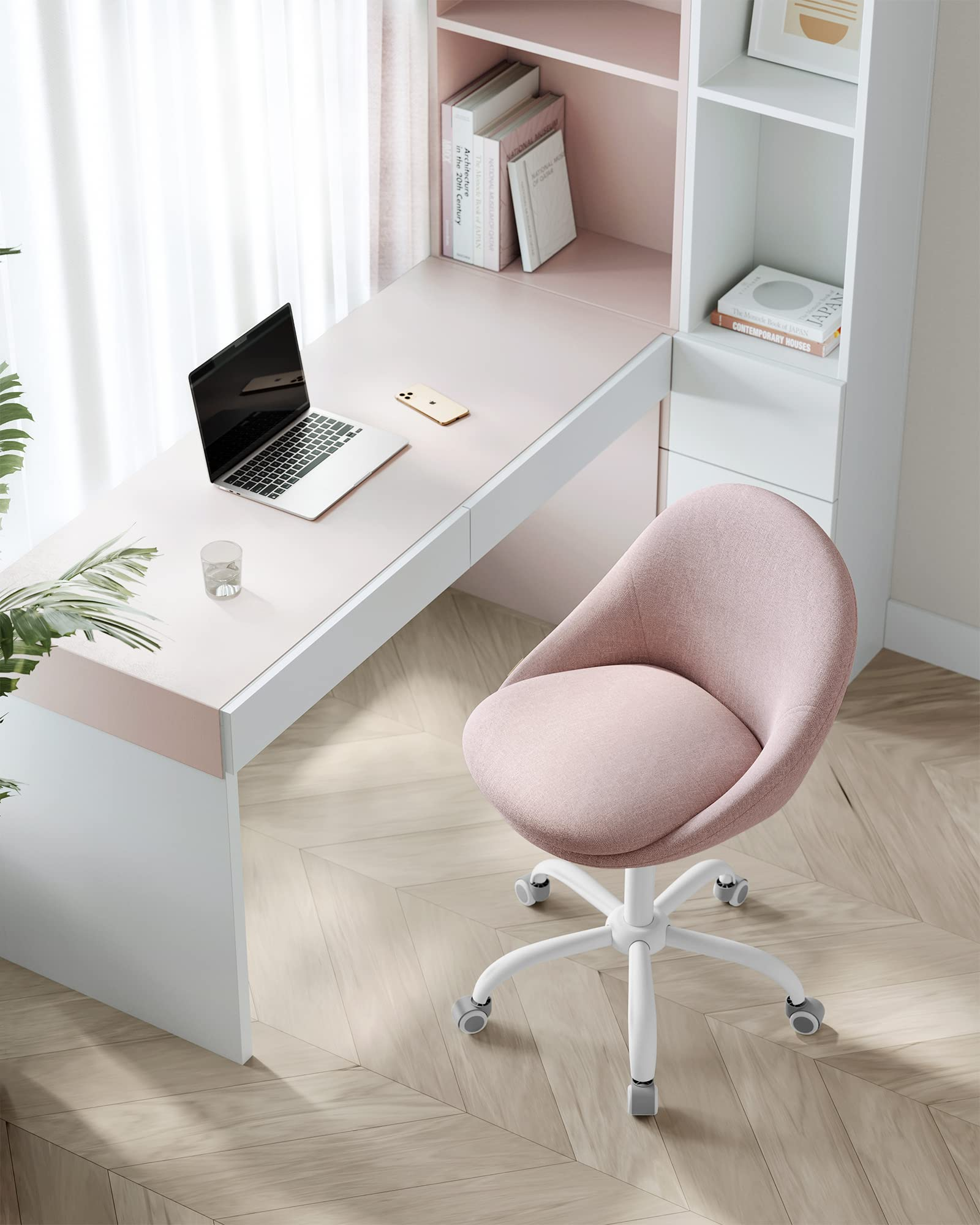 Ein rosafarbener Schreibtisch mit Laptop, ein pinker Drehstuhl, Bücher und ein Fenster mit Vorhängen auf hellem Parkett.