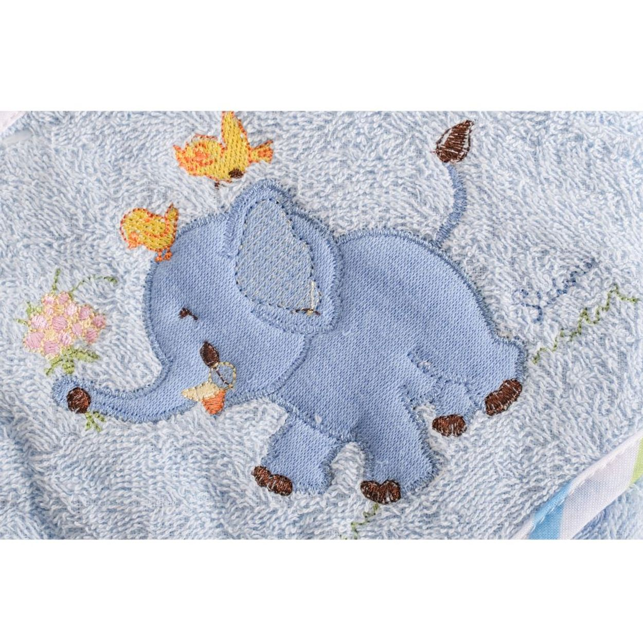 Ein gestickter blauer Elefant hält Blumen mit zwei gelben Vögeln vor hellblauem Hintergrund.
