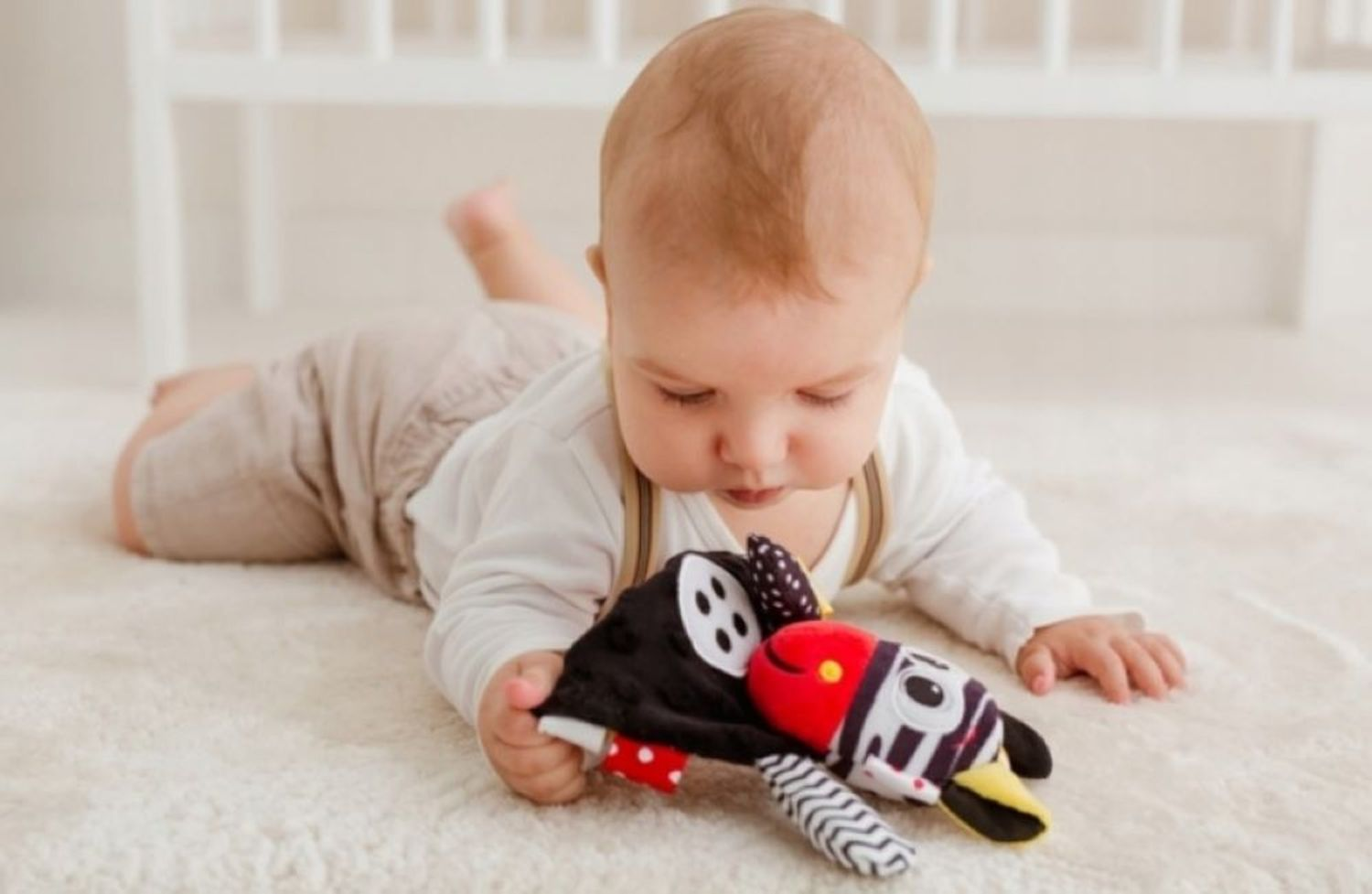 Ein Baby liegt auf einem weißen Teppich und spielt mit einem schwarz-weißen Spielzeug.