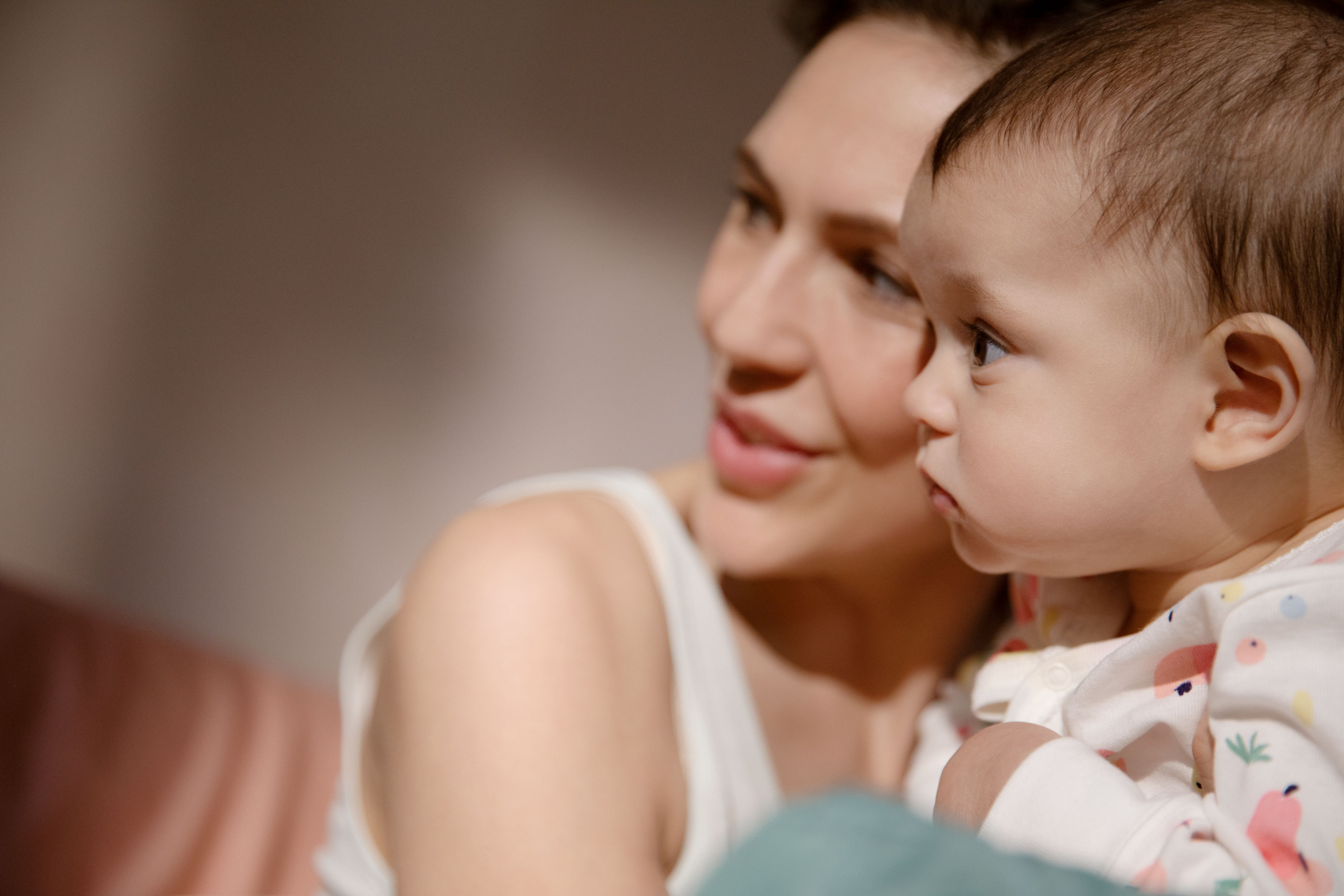 Una donna con un top bianco tiene un bambino in braccio e guardano di lato.