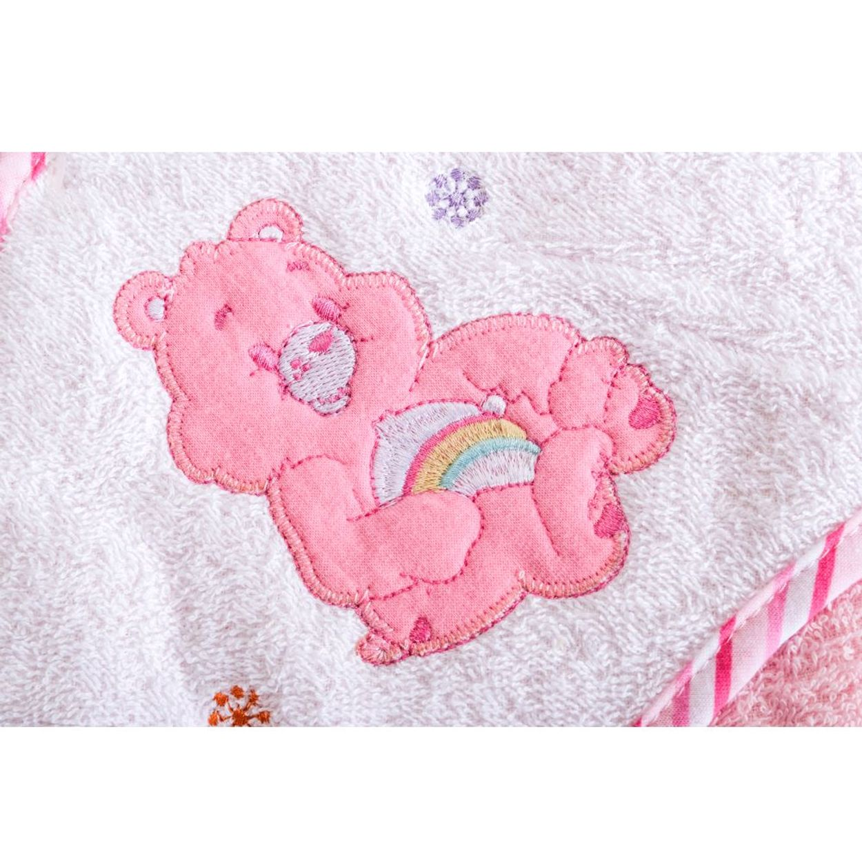 Ein rosafarbener Plüschbär mit einem Regenbogen ist auf ein weißes Handtuch gestickt.