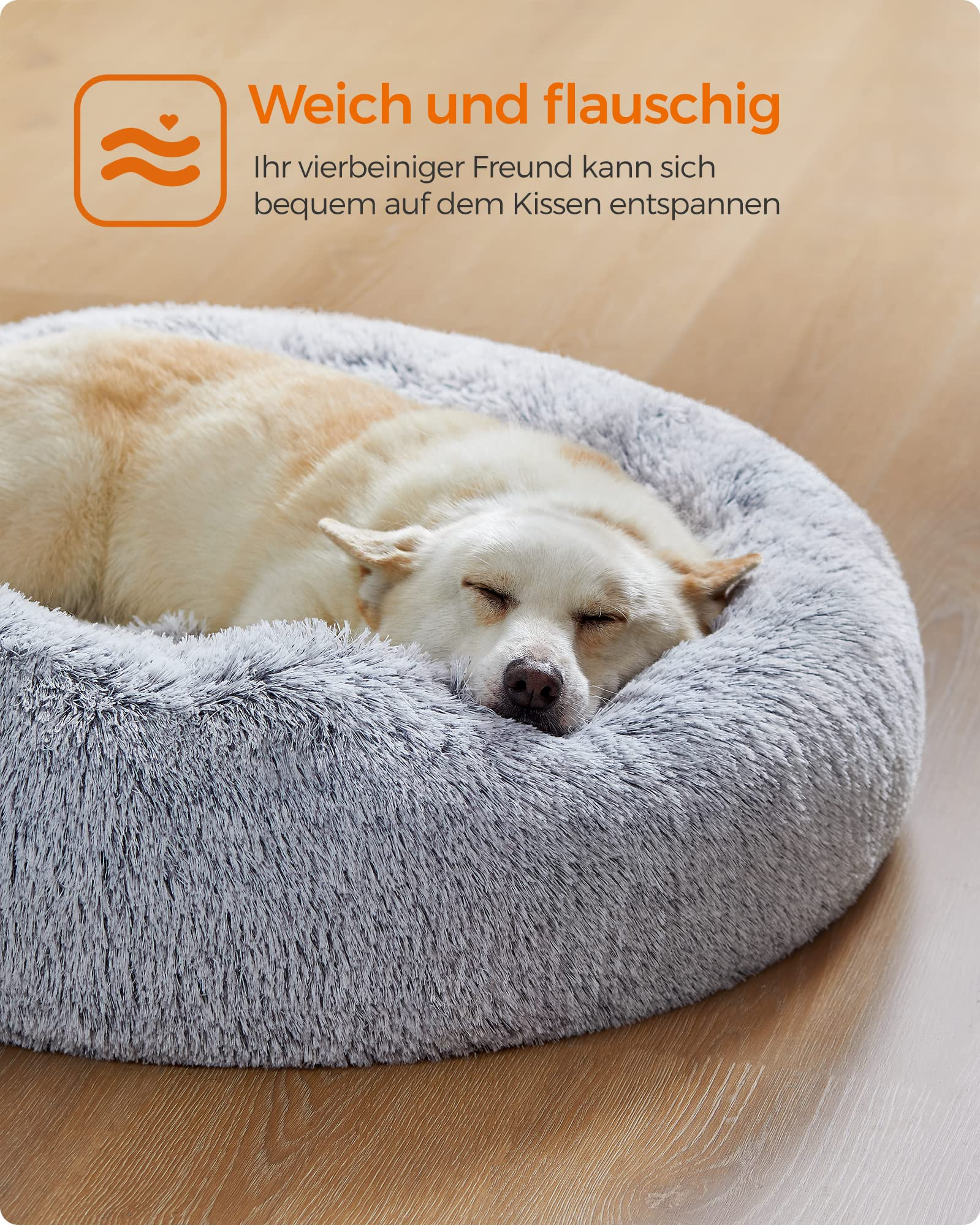 Un chien blanc et marron dort paisiblement dans un lit rond et moelleux gris sur un sol en bois.