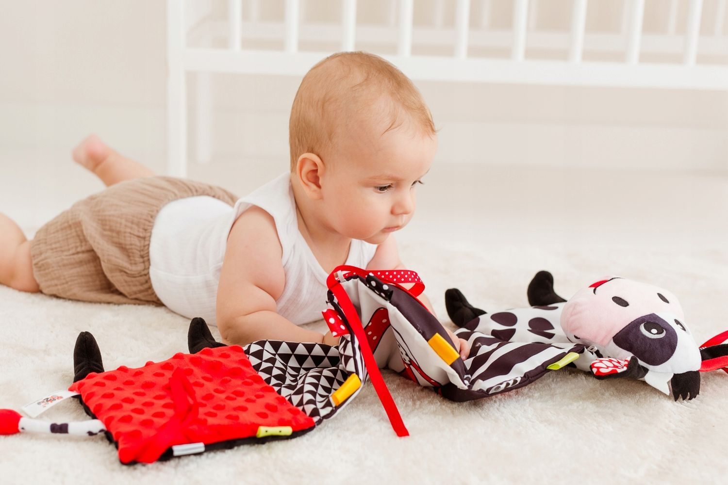 Ein Baby liegt auf dem Bauch auf einem Teppich und spielt mit einem schwarz-weißen Plüschtier.
