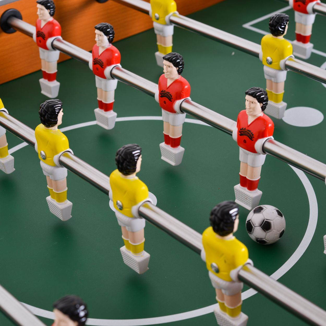 Nahaufnahme eines Tischkickers mit roten und gelben Spielerfiguren auf greenen Spielfeld mit Ball.