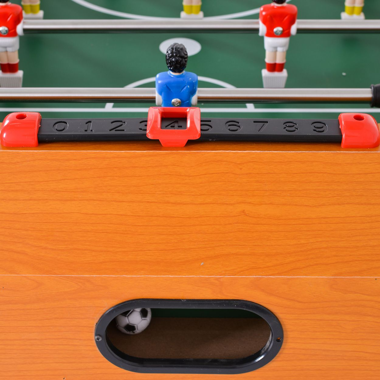 Nahaufnahme eines Tischkicker-Spiels mit einem Ball im Tor und rotem Spielstandszähler auf Holz.