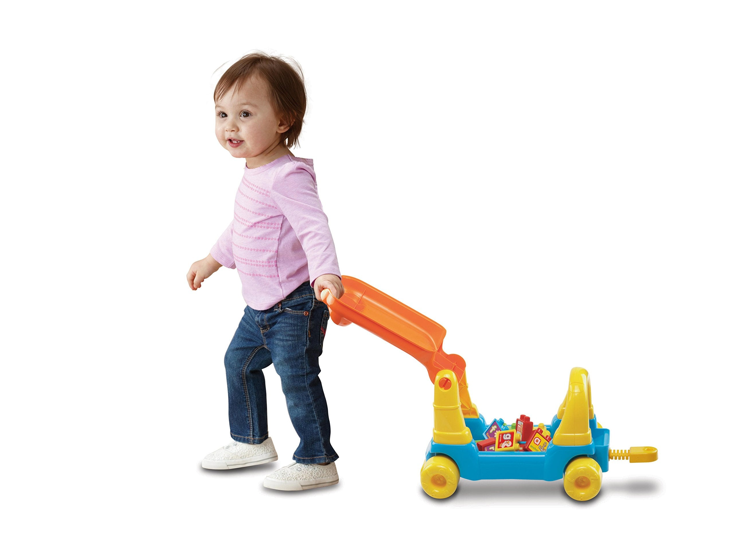 Ein kleiner Junge im rosa Hemd zieht ein blau-gelbes Spielzeugauto mit bunten Bausteinen auf weißem Hintergrund.