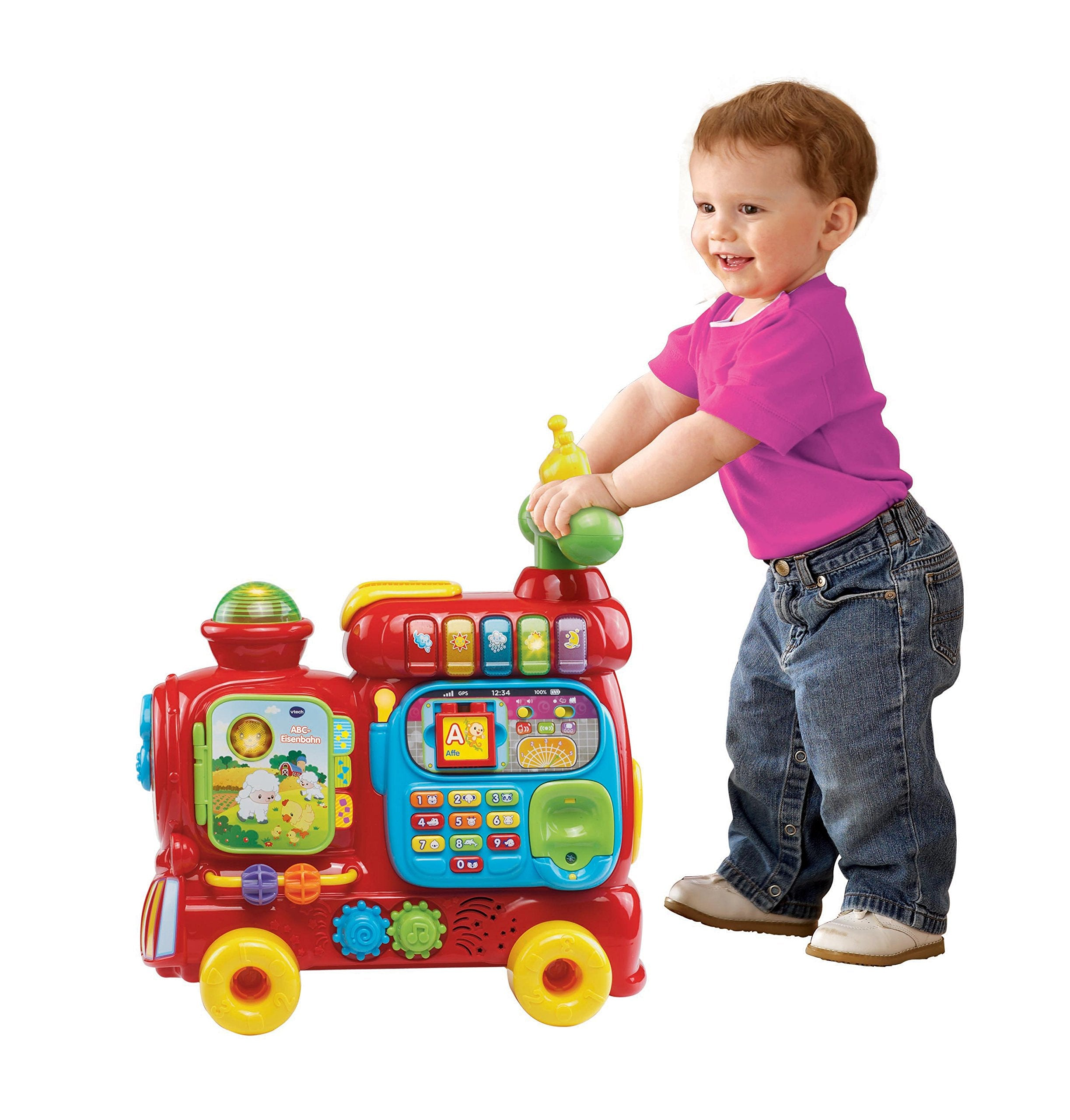 Kleinkind in rosa Shirt und Jeans spielt mit einem bunten Spielzeugzug mit Lichtern und Tasten.
