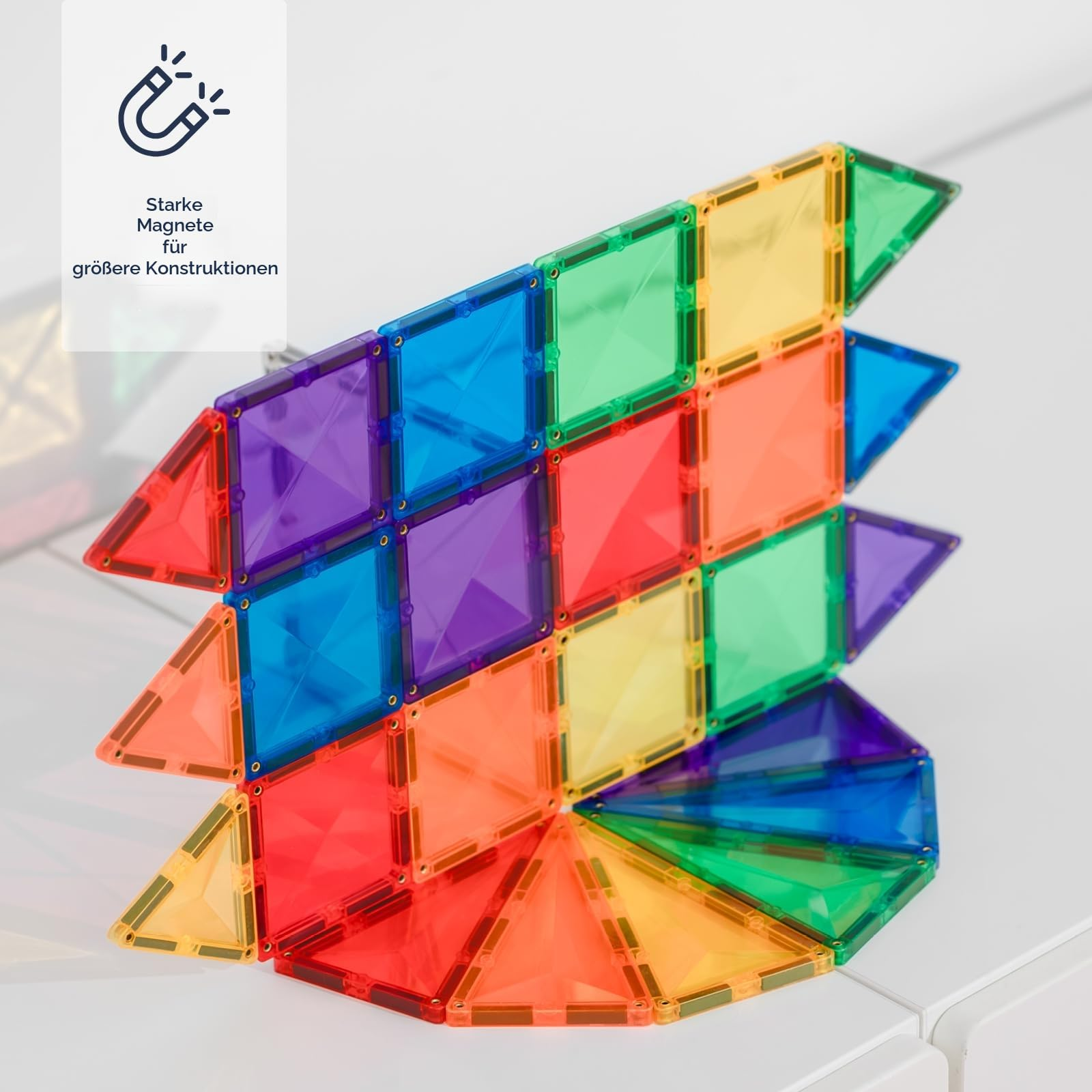 Bunte, transparente Magnetspielzeug-Formen aufgebaut zu einer komplexen Struktur auf einem weißen Tisch.