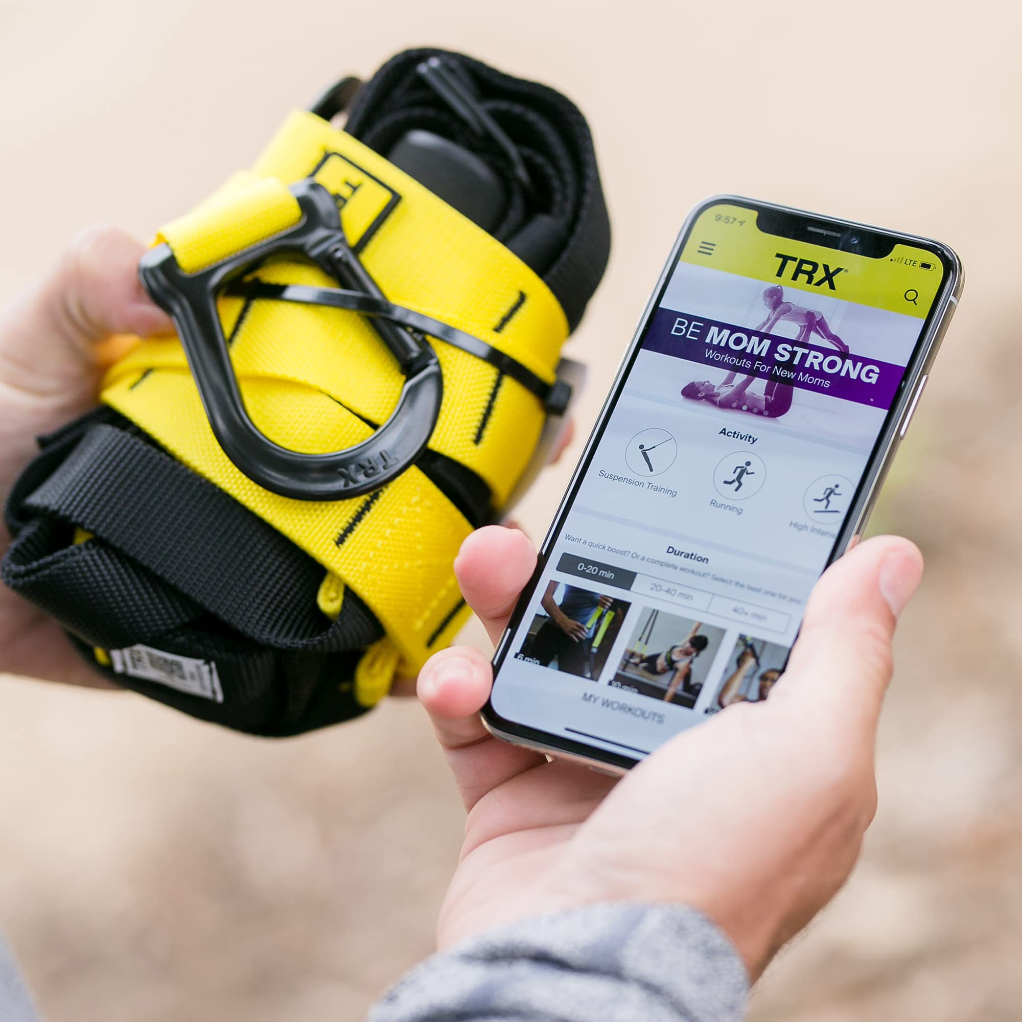 Una persona tiene in mano cinghie di sospensione TRX gialle e nere e uno smartphone con un'app fitness nell'altra.