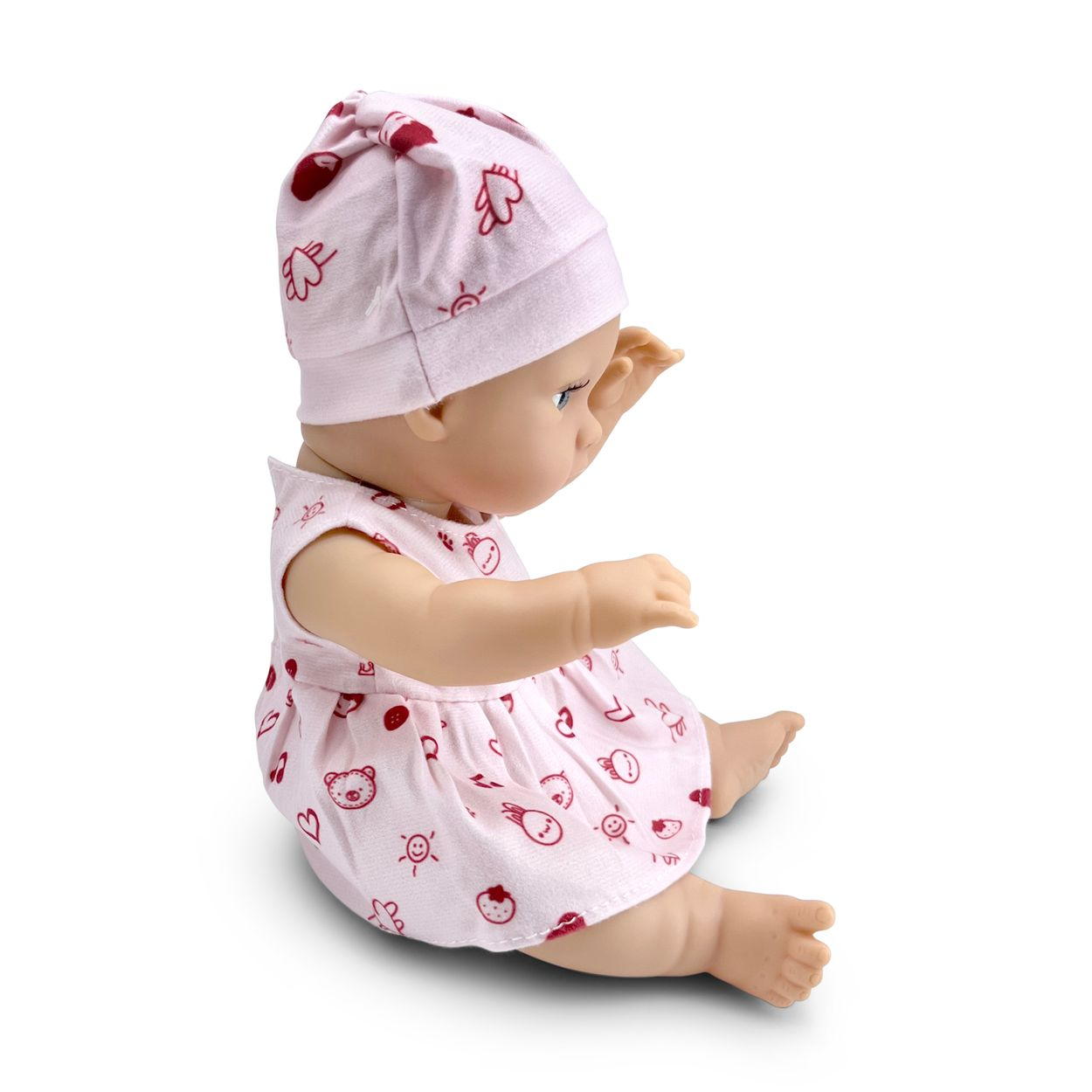 Eine sitzende Babypuppe in einem pinken Kleid und passender Mütze vor weißem Hintergrund.