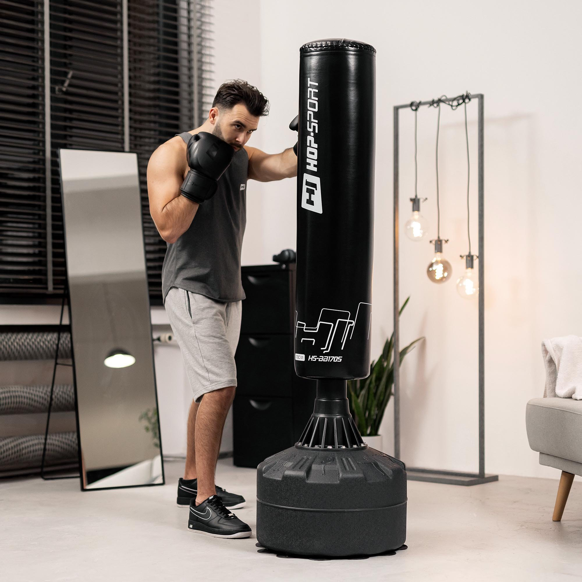 Ein Mann in Sportkleidung und Boxhandschuhen boxt in einem hellen Raum gegen einen freistehenden Boxsack.