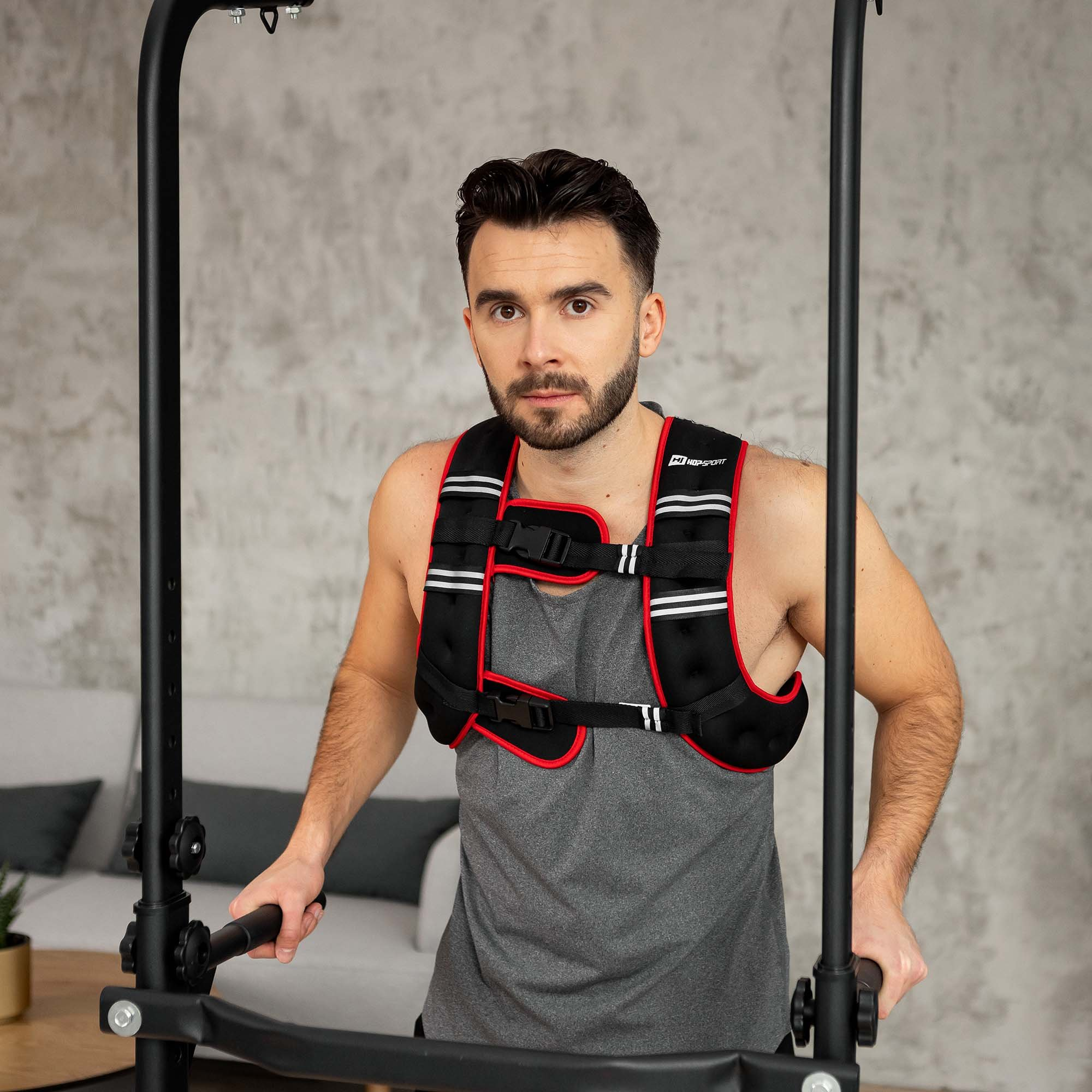 Ein Mann mit Bart trägt eine schwarze Gewichtsweste und steht zwischen Fitnessstangen.