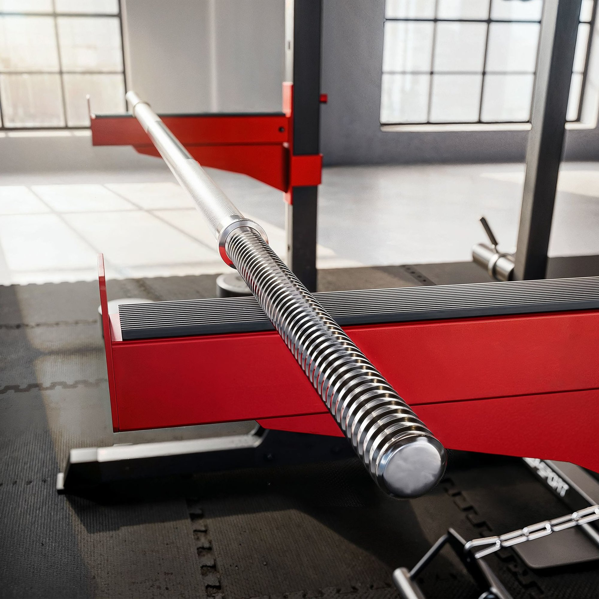 Eine Nahaufnahme einer silbernen Langhantelstange auf einer roten Hantelbank in einem Fitnessstudio.