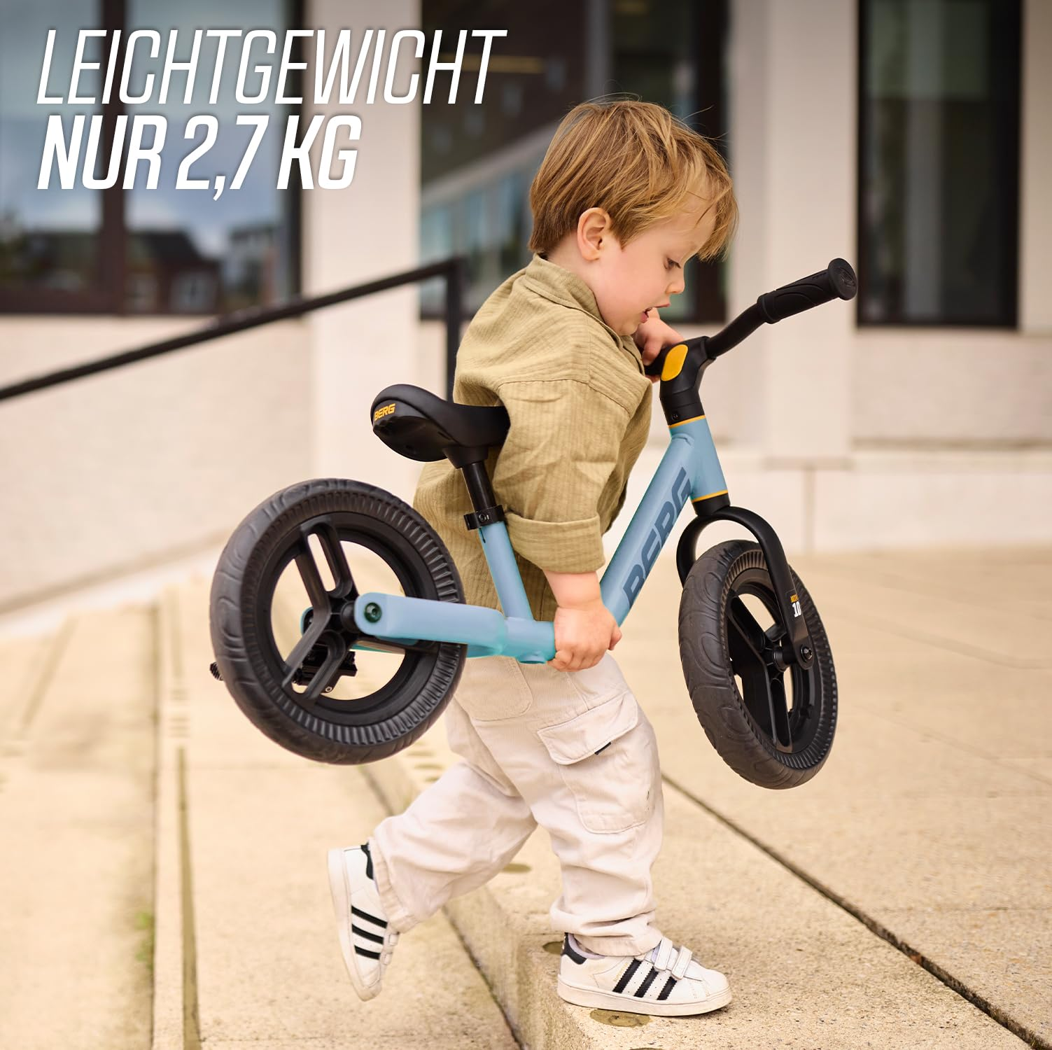 Un bambino trasporta una bici senza pedali azzurra e nera giù per le scale.