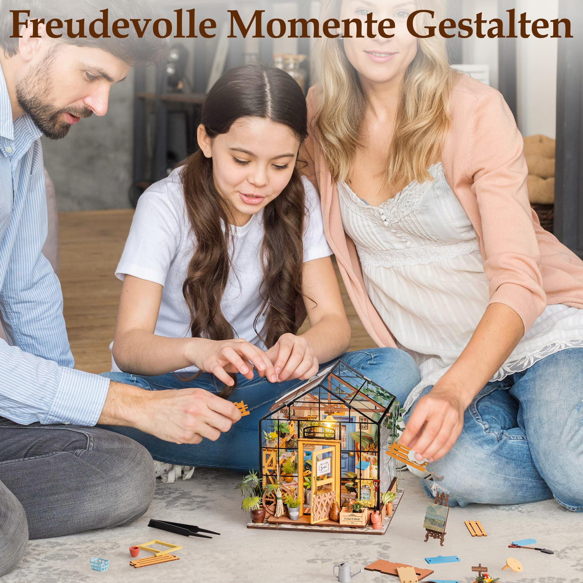 Eine dreiköpfige Familie sitzt auf dem Boden und baut zusammen ein kleines Holzgewächshaus auf.