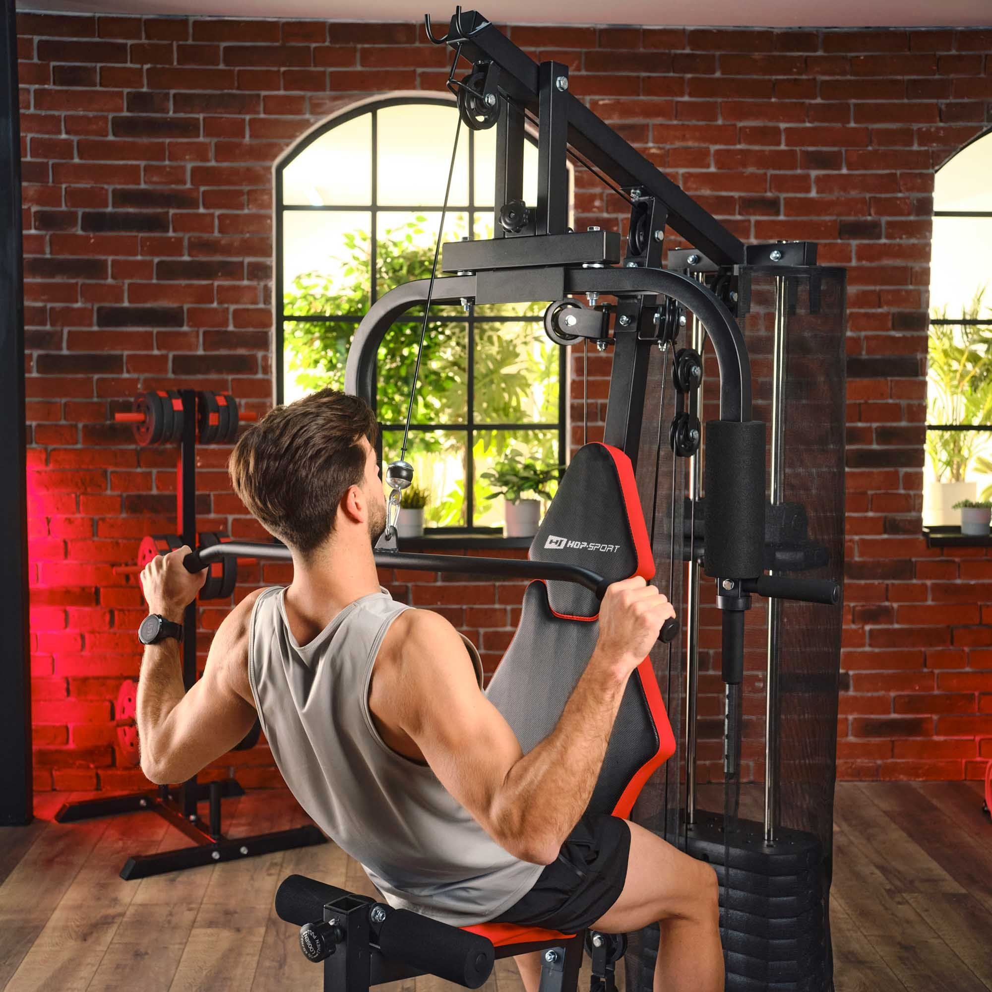 Ein Mann in einem Fitnessstudio trainiert an einer Kraftstation vor einer Ziegelwand.