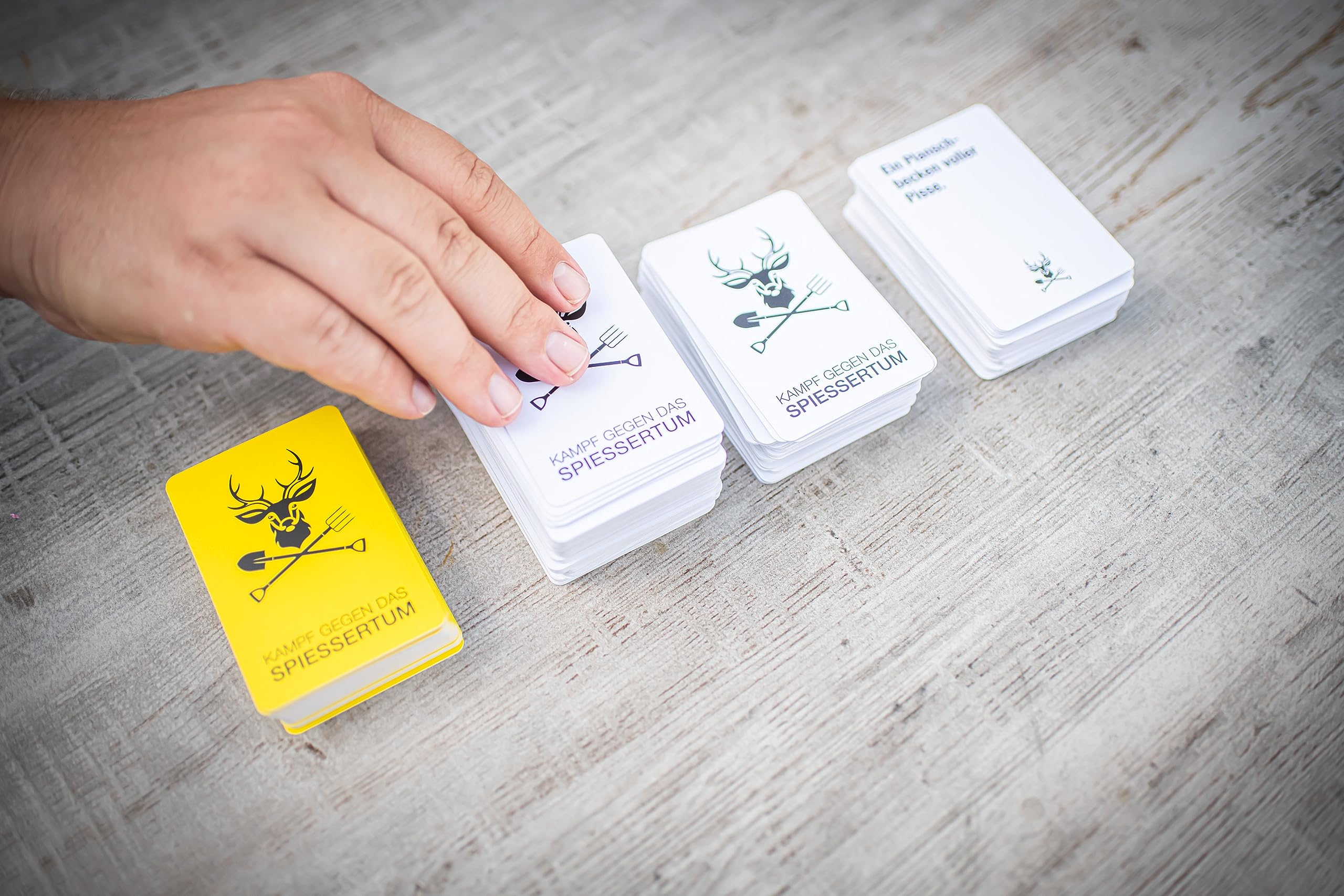 Une main touche une pile de cartes de jeu blanches sur une table en bois près d'un jeu jaune.